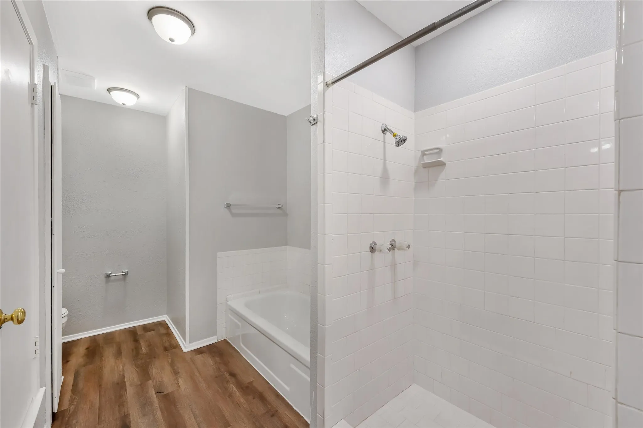 Bathroom featuring a white subway tile shower, built-in bathtub, and wood-finish flooring