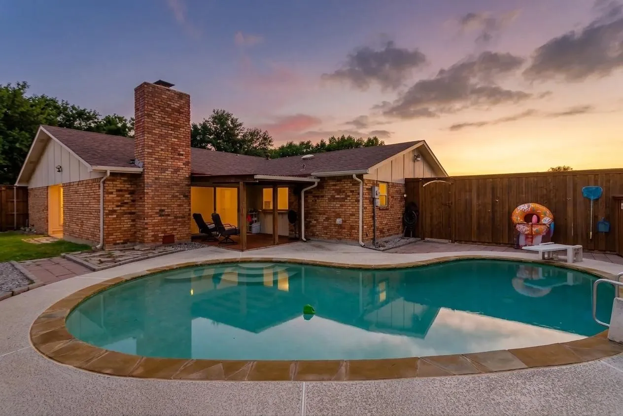 Freeform swimming pool with a stone coping border, surrounded by textured concrete decking