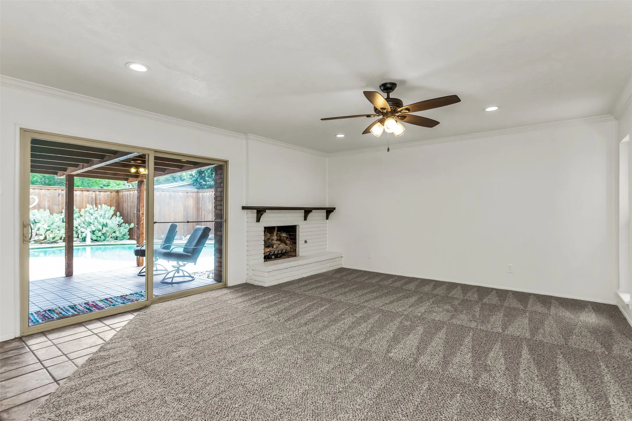 Expansive living area featuring patterned carpeting, a white brick fireplace with a dark wood mantel, and a ceiling fan with integrated lighting