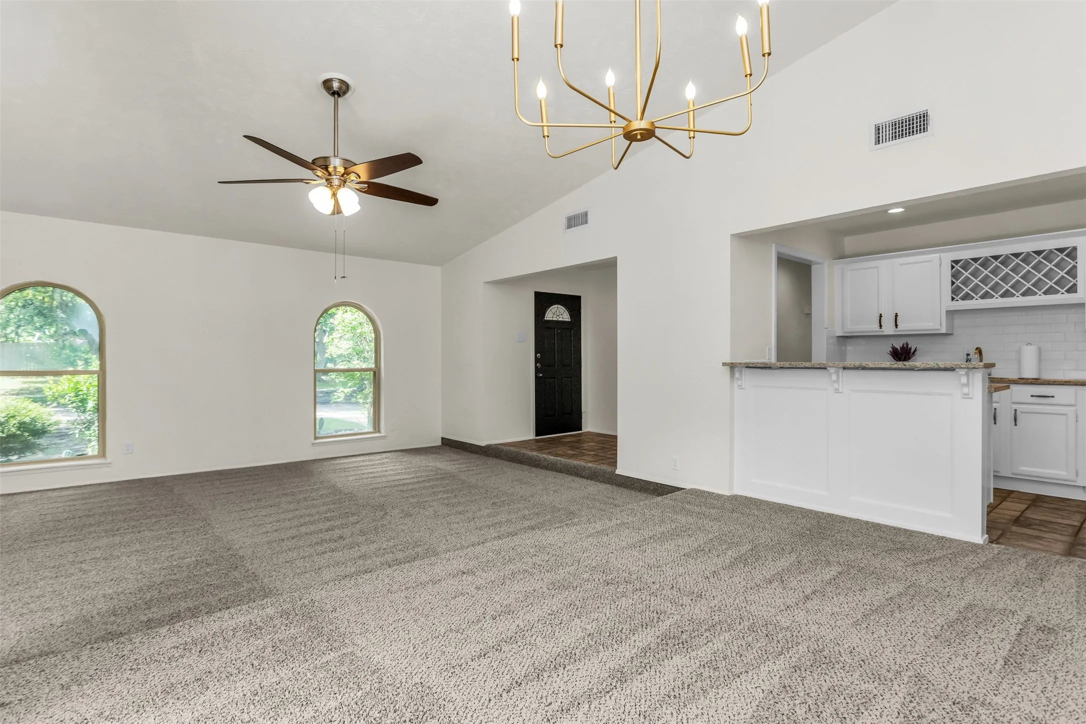 Vaulted ceiling living area featuring arched windows, a modern chandelier, and a ceiling fan