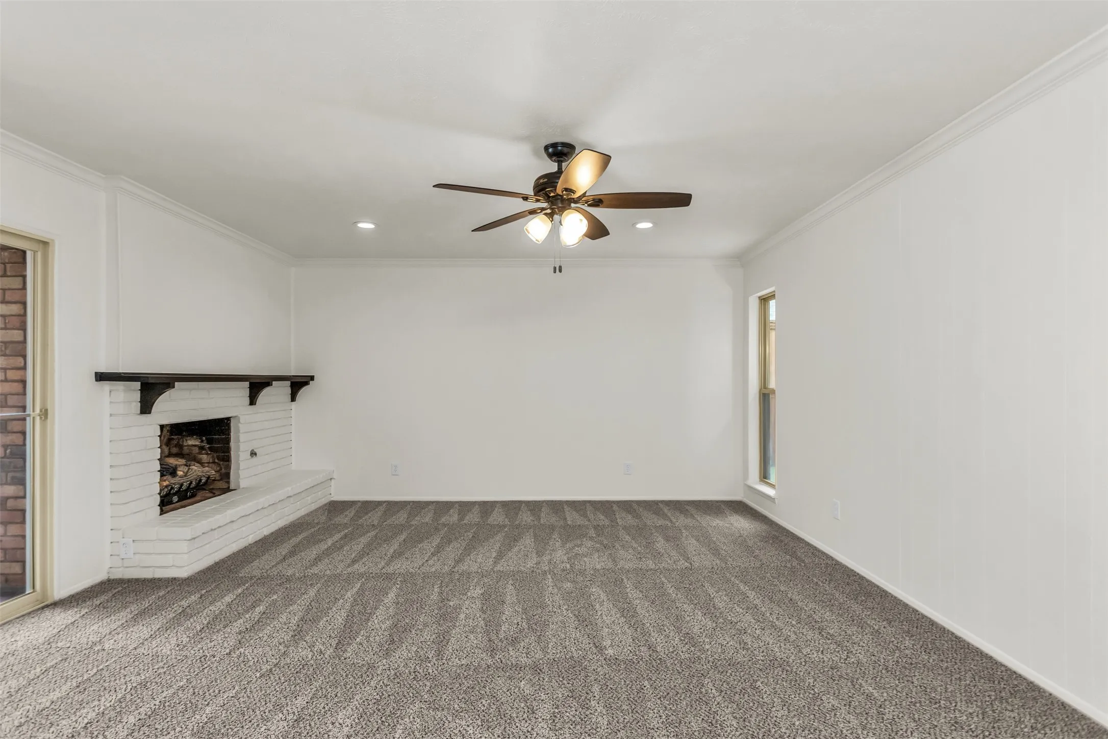 Spacious room featuring a white brick fireplace with a dark mantle, patterned carpeting, and crown molding