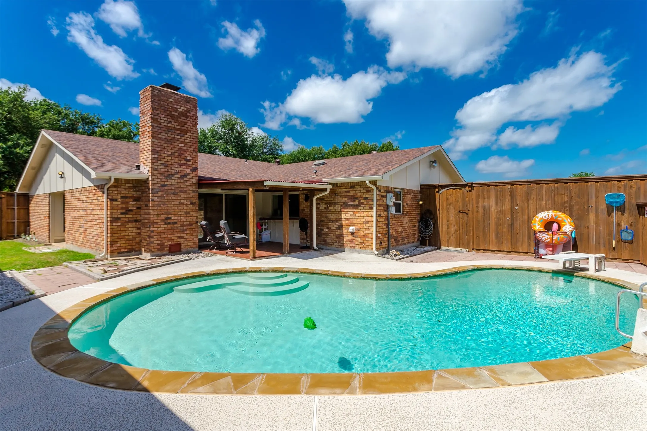 Freeform swimming pool with integrated steps, surrounded by a light-colored aggregate deck and natural stone coping