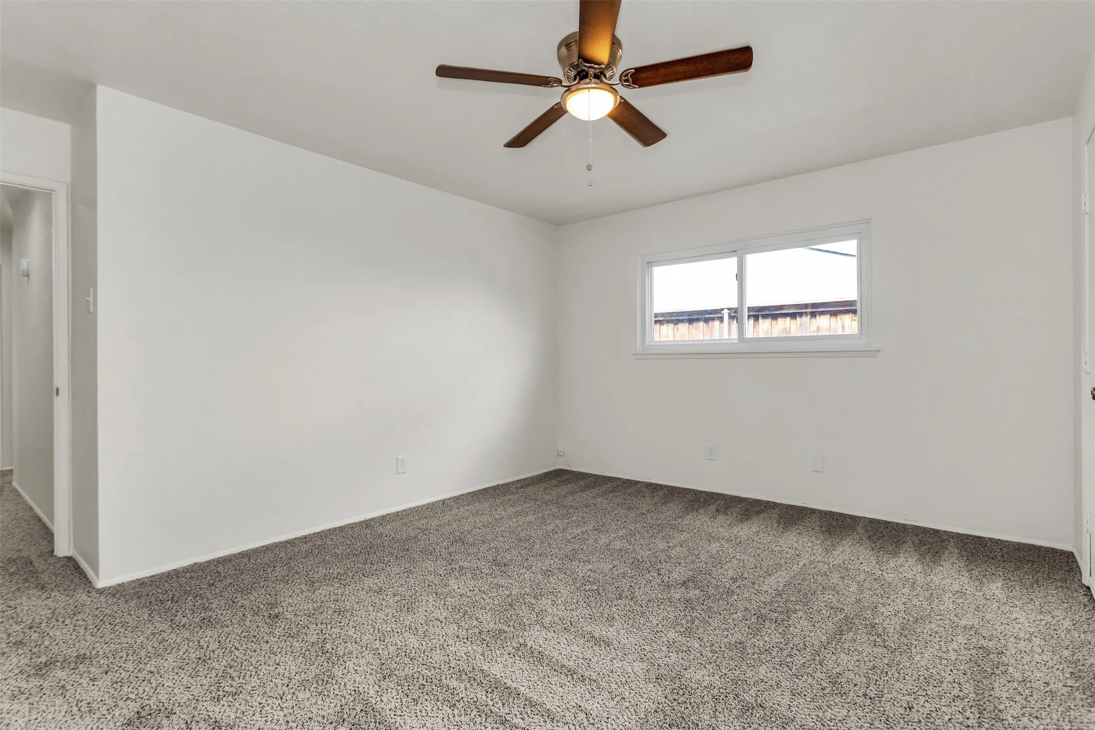 Room featuring plush gray carpeting, white walls, a single window with white trim, and a ceiling fan with integrated lighting