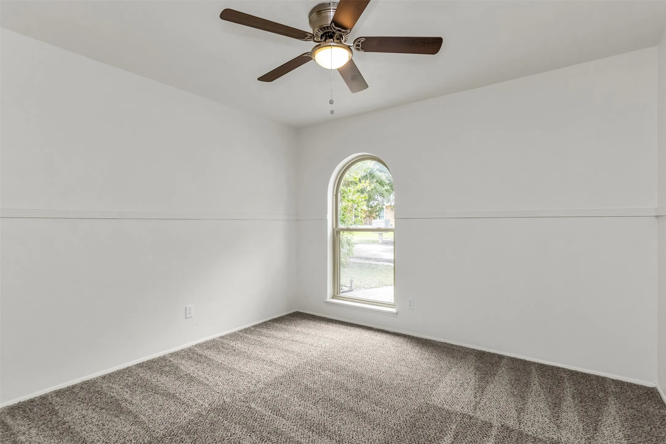 Interior room featuring a contemporary ceiling fan, arched window, neutral wall paint, and gray textured carpeting