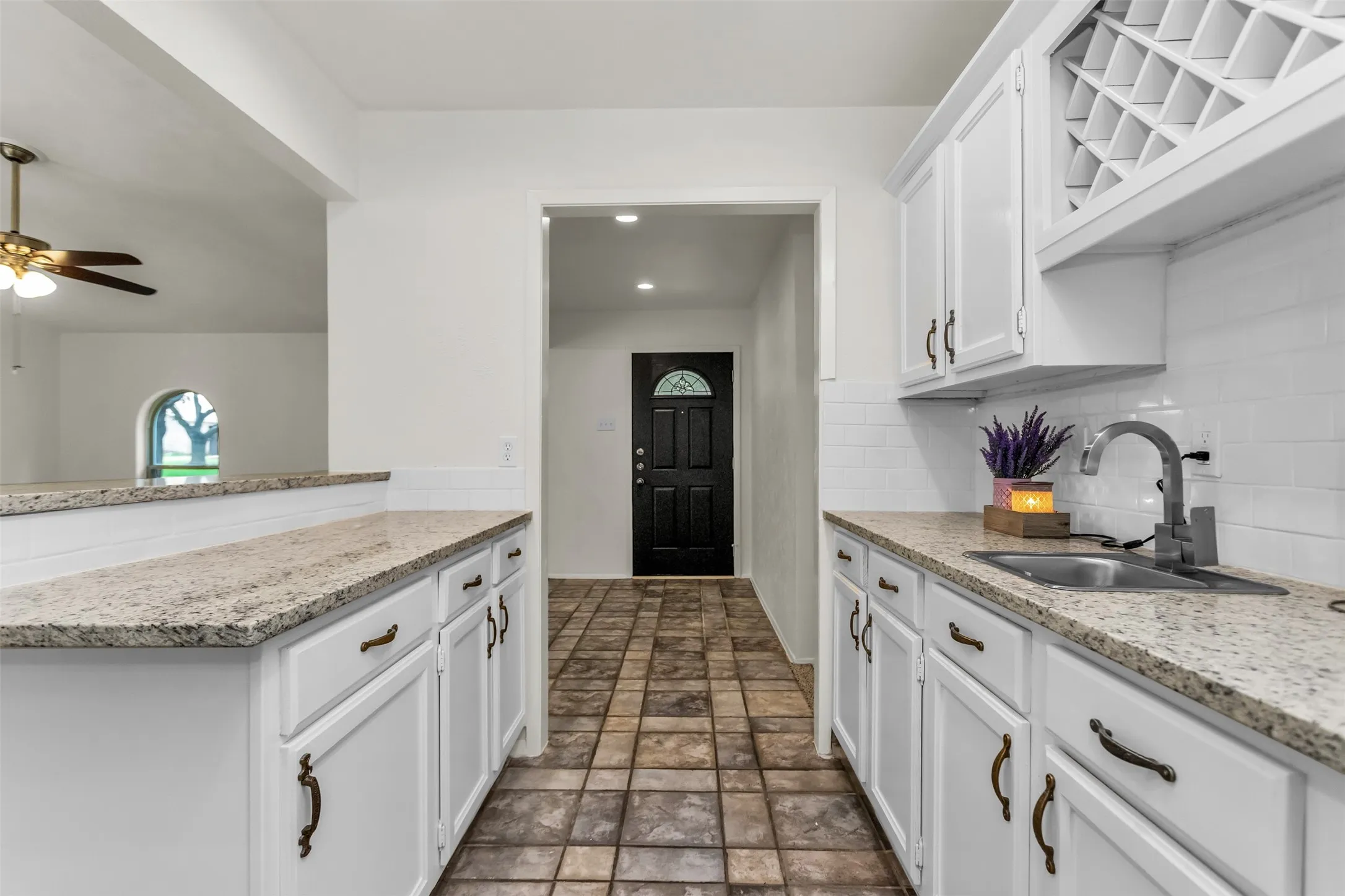 Kitchenette featuring white cabinetry, granite-finish countertops, stainless steel sink with a modern faucet, and a white subway tile backsplash