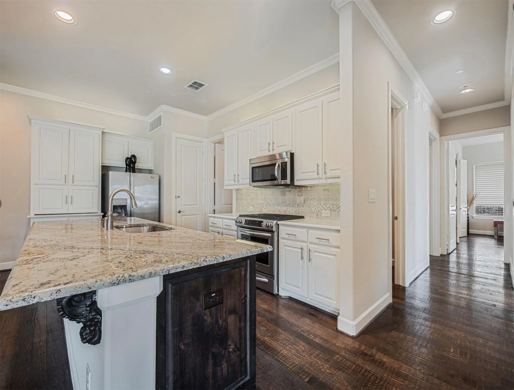 Gourmet kitchen featuring a granite island with an undermount sink, stainless steel appliances, white cabinetry, decorative tile backsplash, and dark wood-finish flooring
