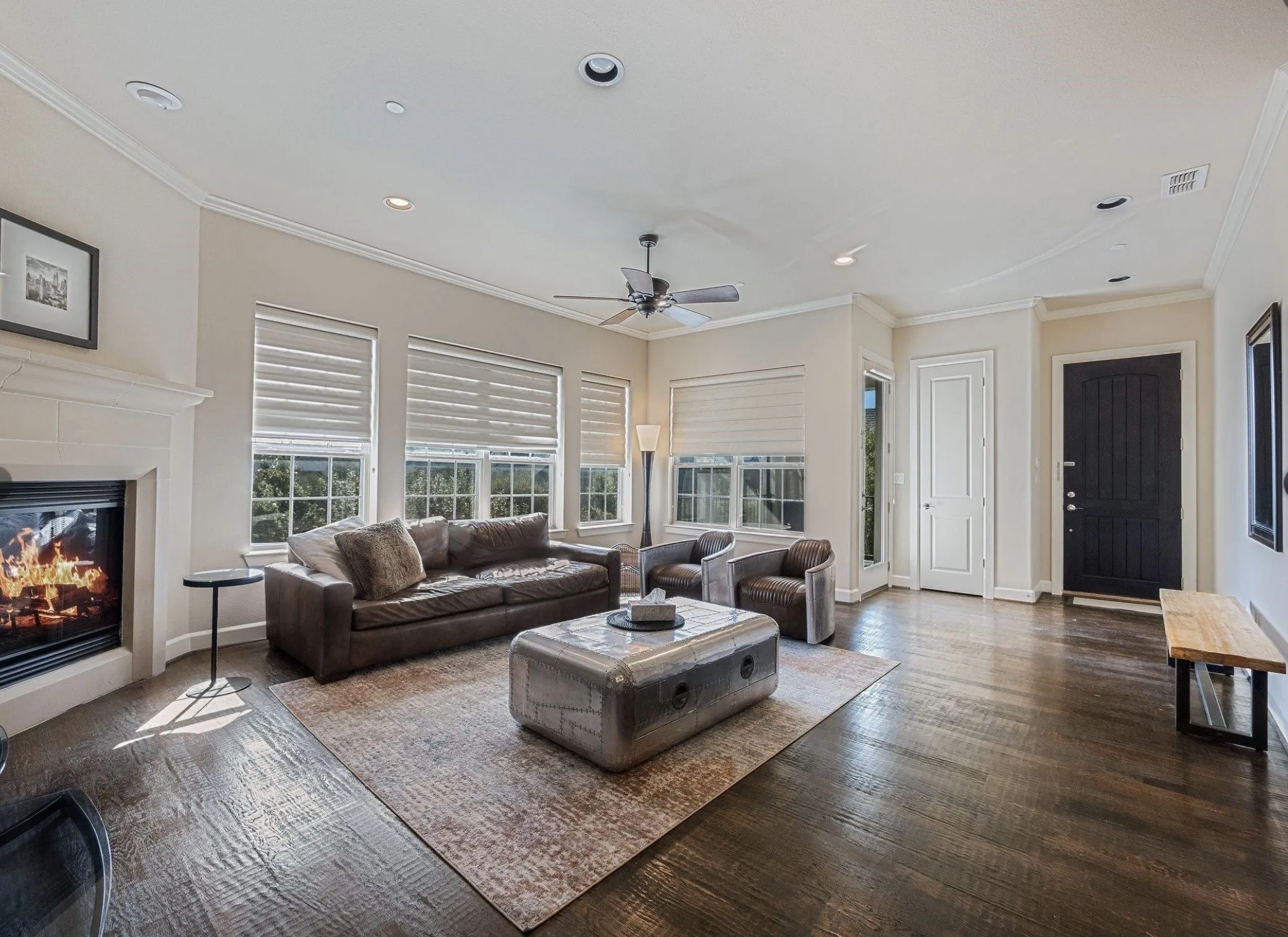 Spacious living area featuring dark wood flooring, a fireplace with a stone surround, multiple windows with blinds, crown molding, and recessed lighting