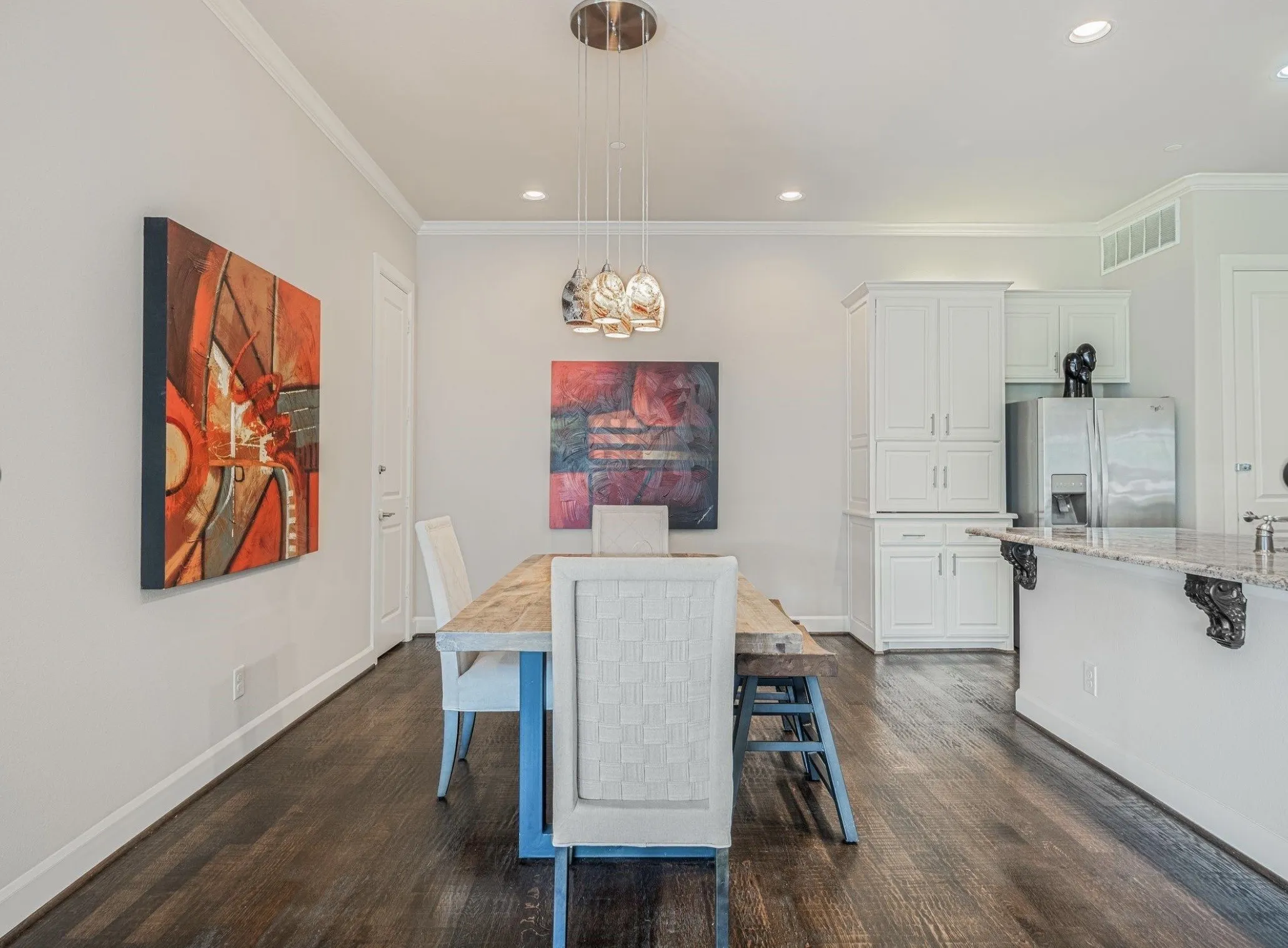 Dining area featuring rich wood-finish flooring, white crown molding, recessed lighting, and a multi-pendant light fixture