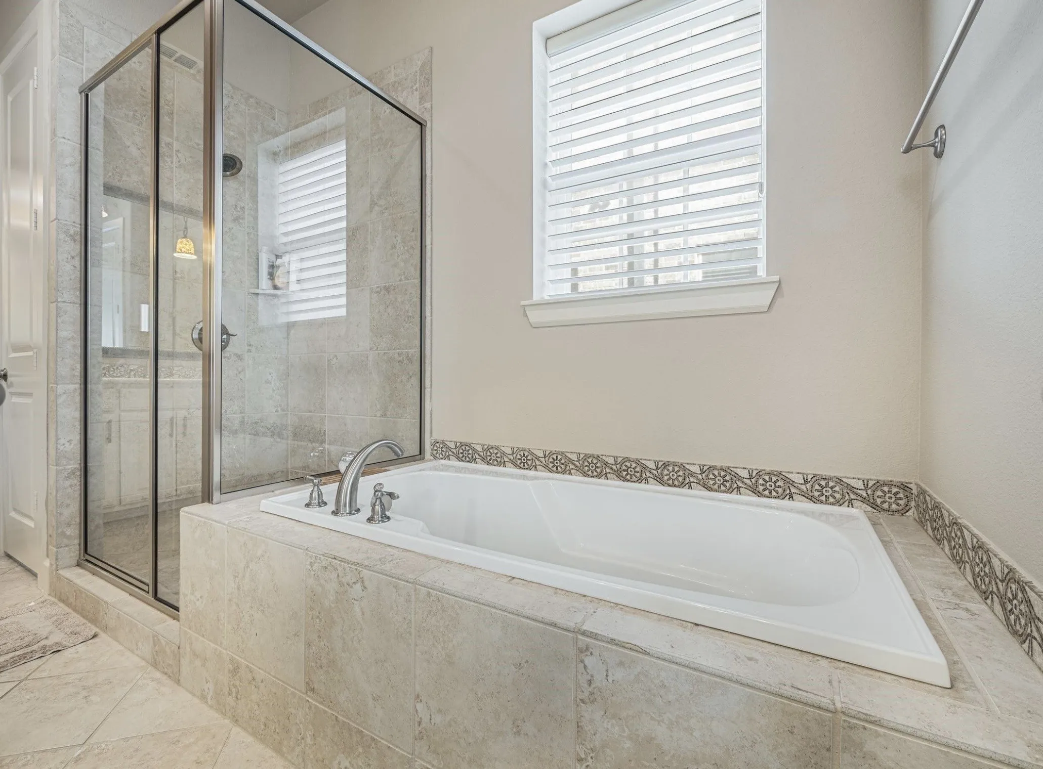Soaking tub with decorative tile surround, complemented by a glass-enclosed shower with tile walls