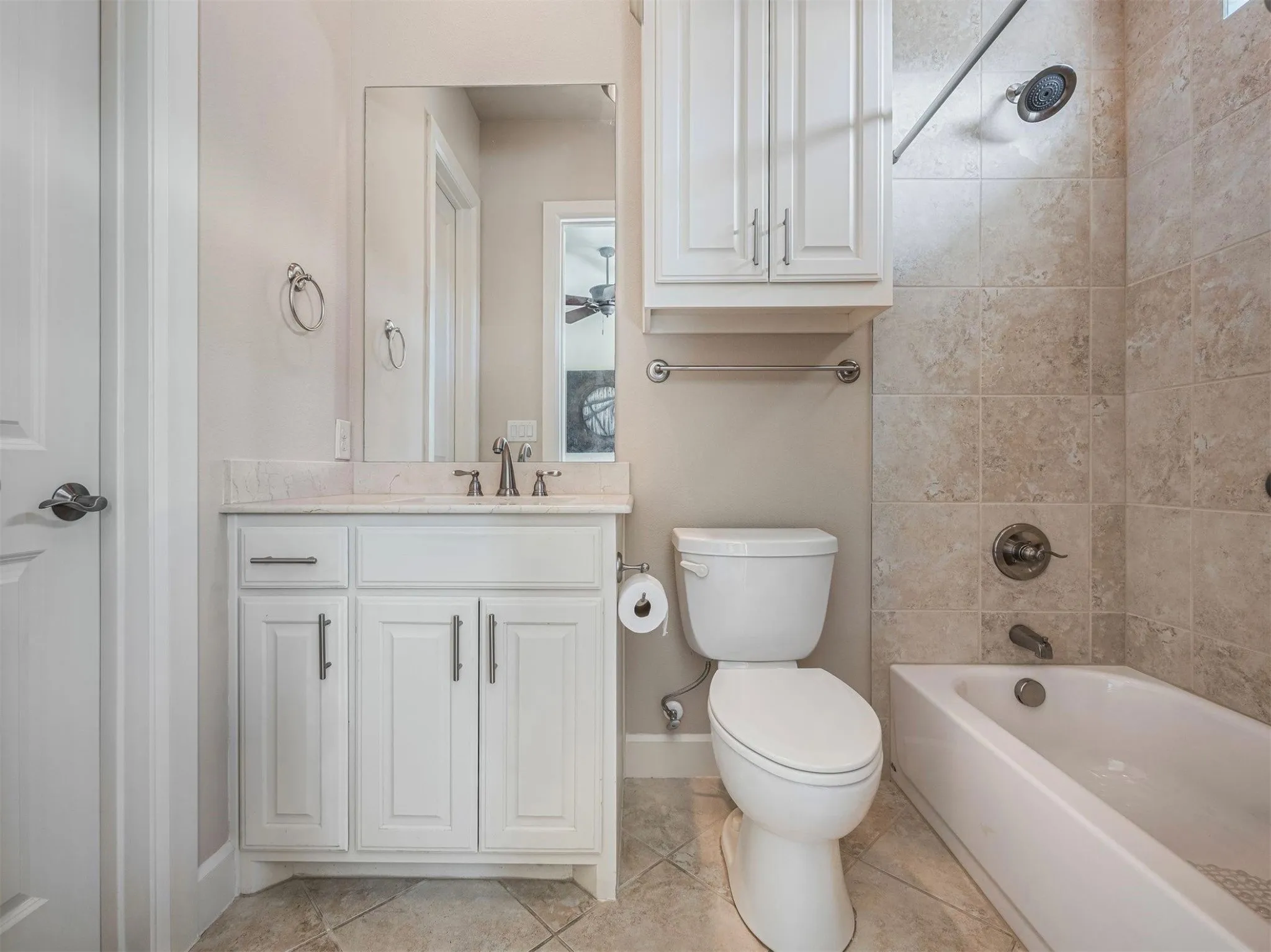 Bathroom featuring a white vanity with a light-colored countertop, ceramic tile flooring, a built-in bathtub with tiled surround, and an overhead storage cabinet