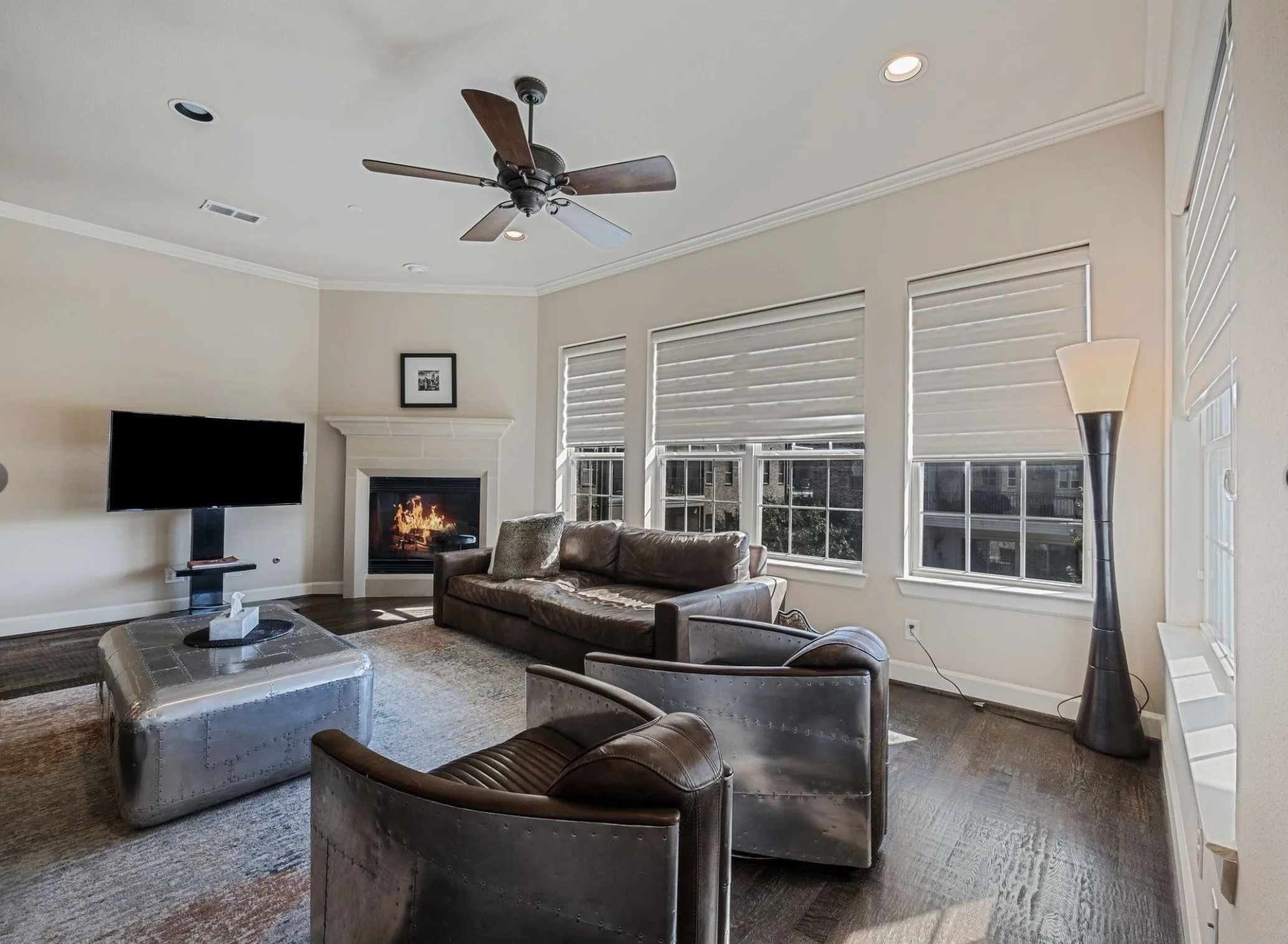 Living area featuring wood-finish flooring, a corner fireplace with a stone mantel, multiple windows with blinds, a ceiling fan, and recessed lighting
