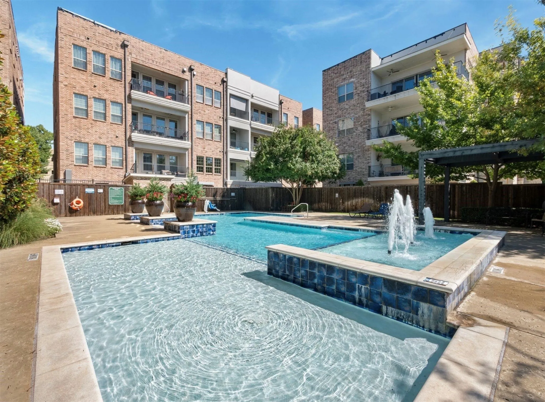 Resort-style pool area featuring a water fountain, blue mosaic tile accents, and a surrounding paved deck