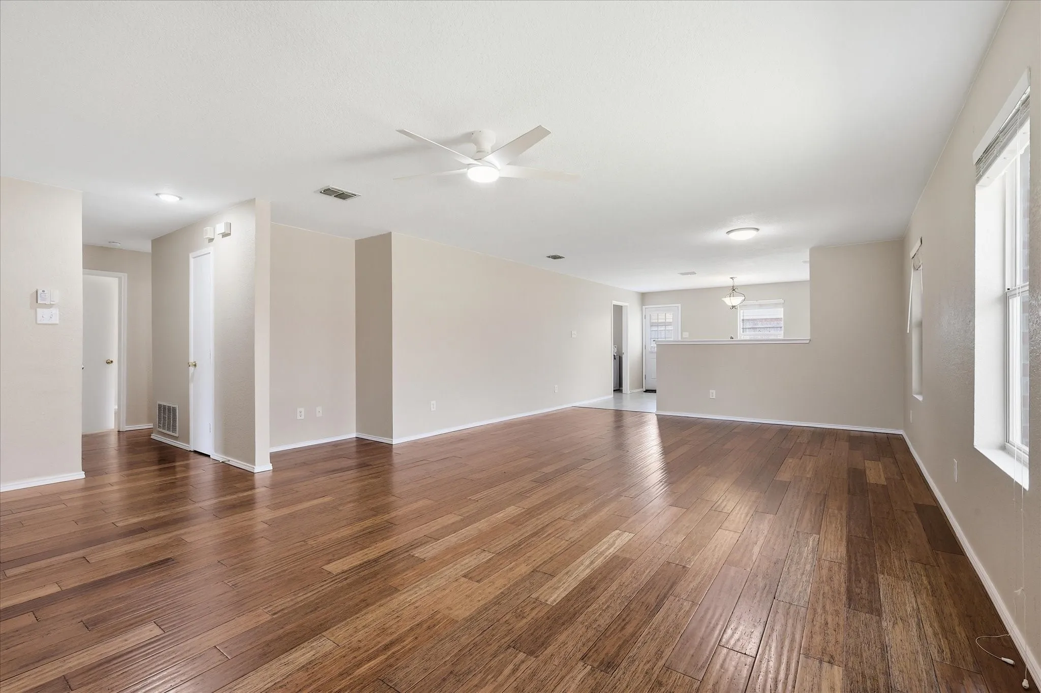 Expansive living area featuring rich wood-finish flooring, neutral wall tones, and multiple windows for natural light