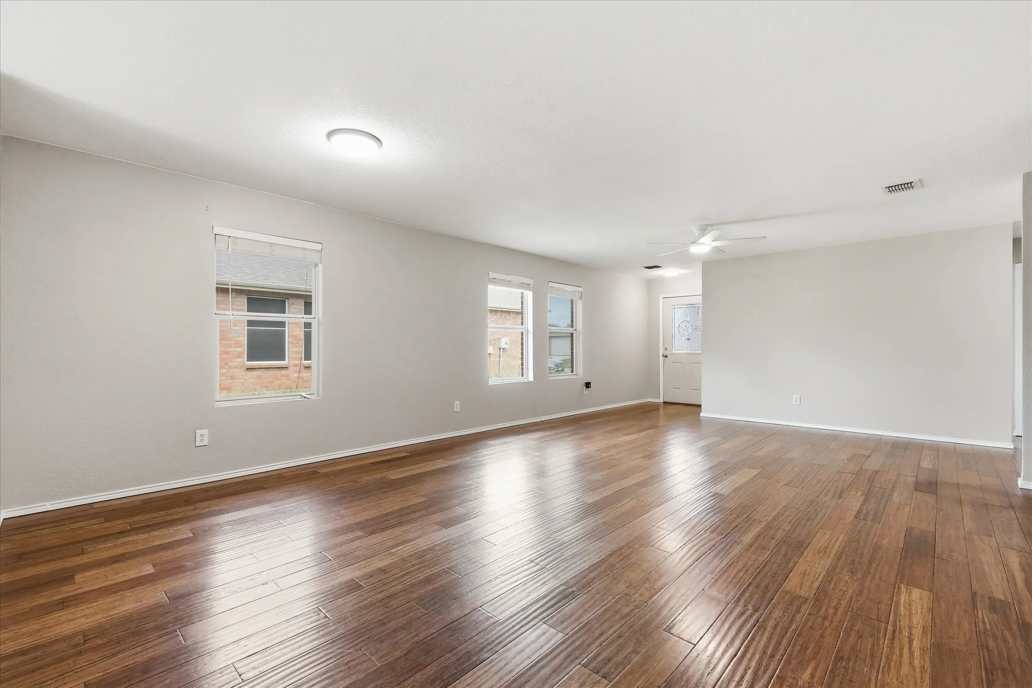 Expansive living area featuring rich wood-finish flooring, neutral wall tones, multiple windows, a ceiling fan, and recessed lighting