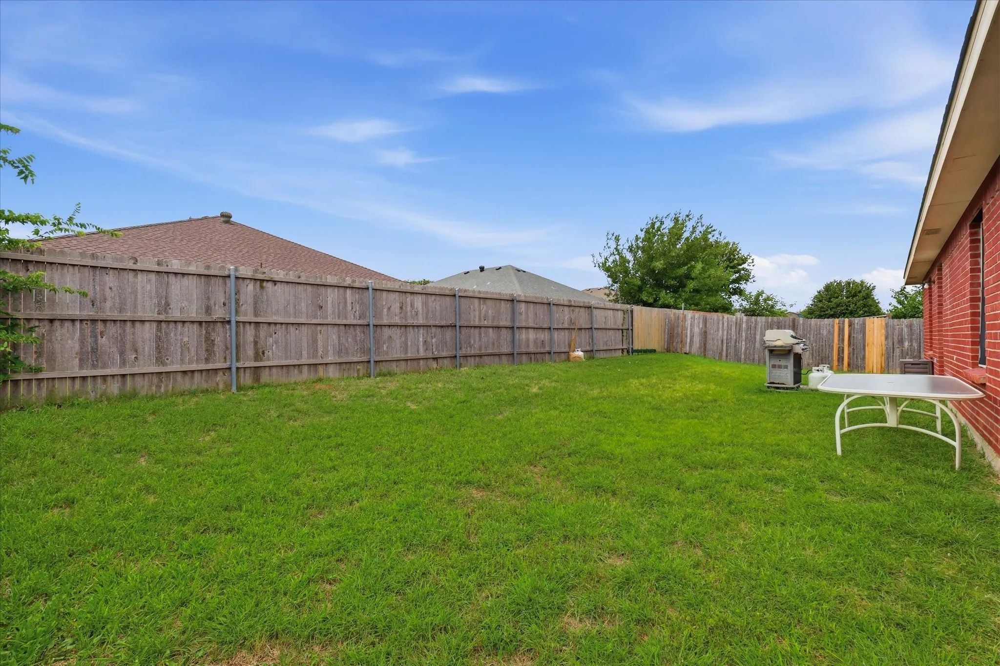 Expansive backyard featuring a manicured lawn, full privacy fencing, and a brick exterior wall