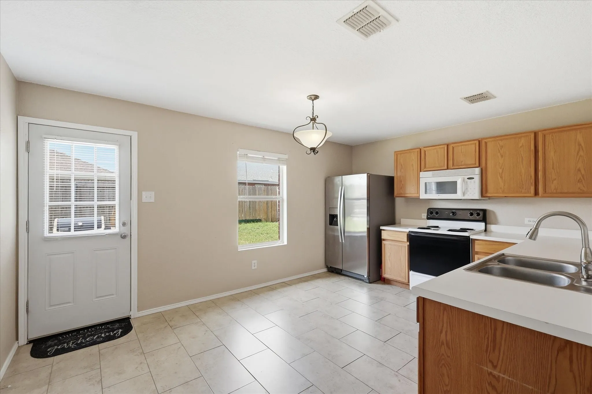 Kitchen featuring wood cabinetry, white countertops, tile flooring, a double basin sink with a high-arc faucet, and an overhead lighting fixture