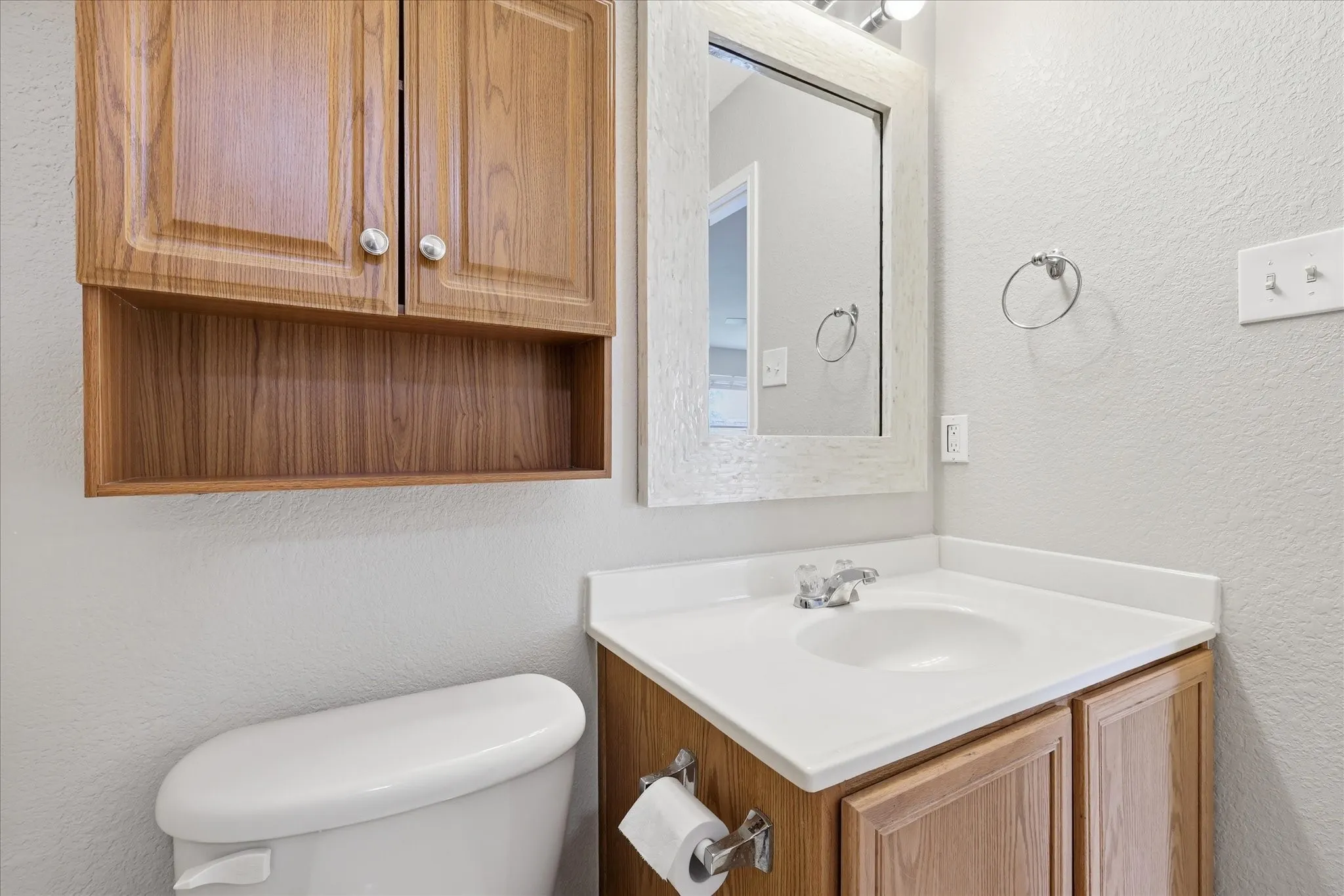 Bathroom featuring a white toilet, wood-finish vanity with an integrated sink, and a framed mirror