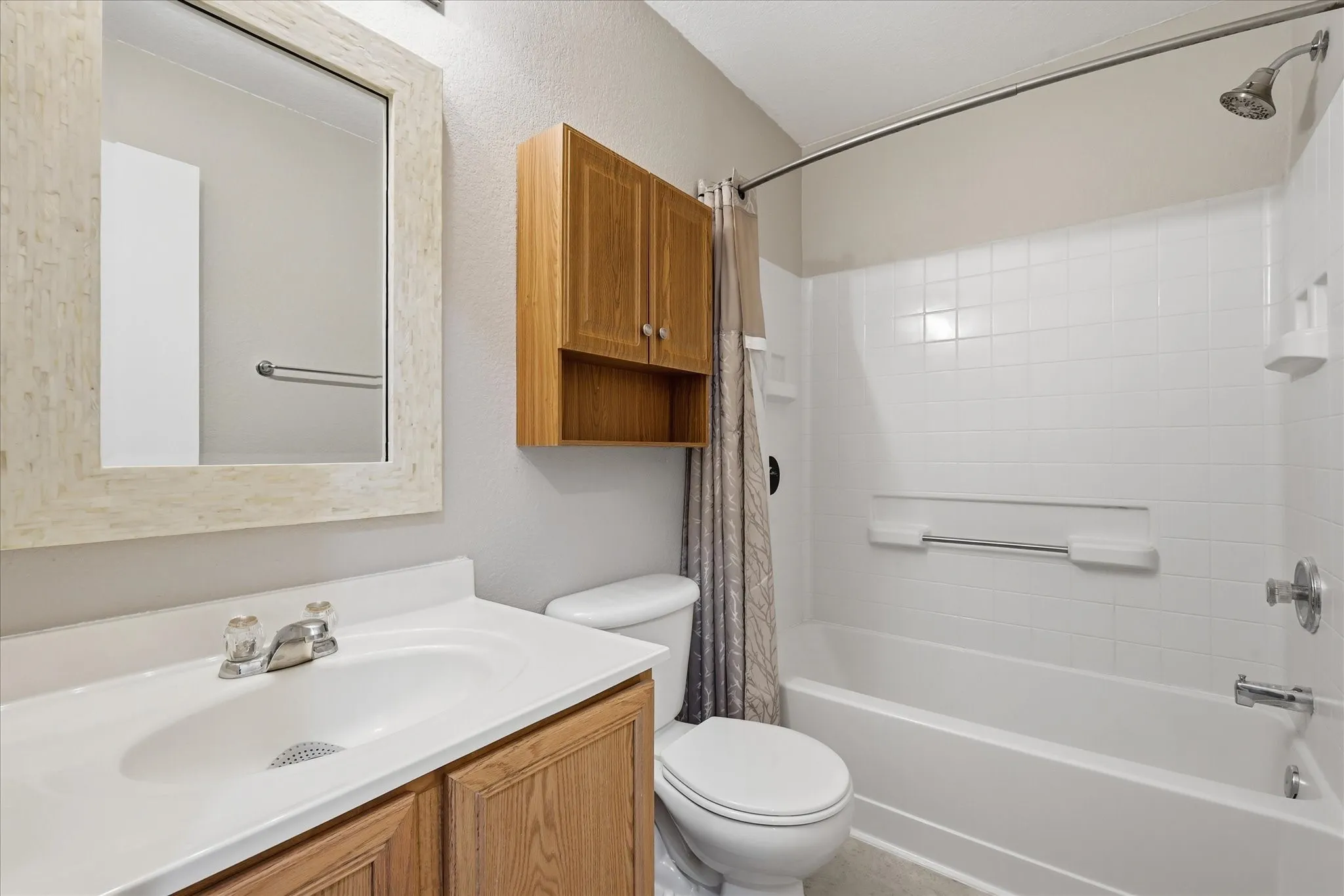 Bathroom featuring a white bathtub with tile surround, a single vanity with wood-finish cabinetry and an integrated sink, a framed mirror, and a wall-mounted wood-finish cabinet