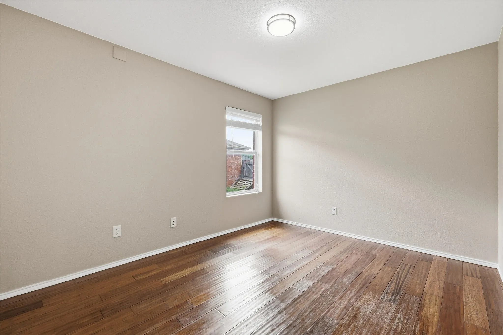 Spacious room featuring wood-finish flooring, neutral-toned walls, and a single window with blinds