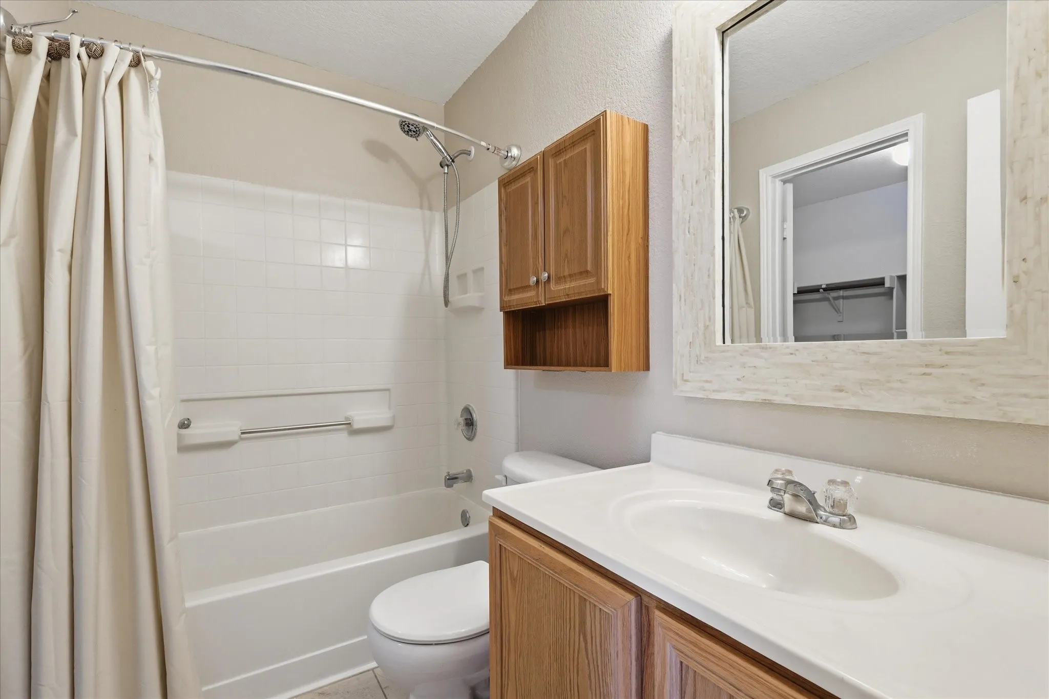 Bathroom featuring a white bathtub with tile surround, a built-in shower fixture, a vanity with an integrated sink, a wood-finish cabinet, and a framed mirror