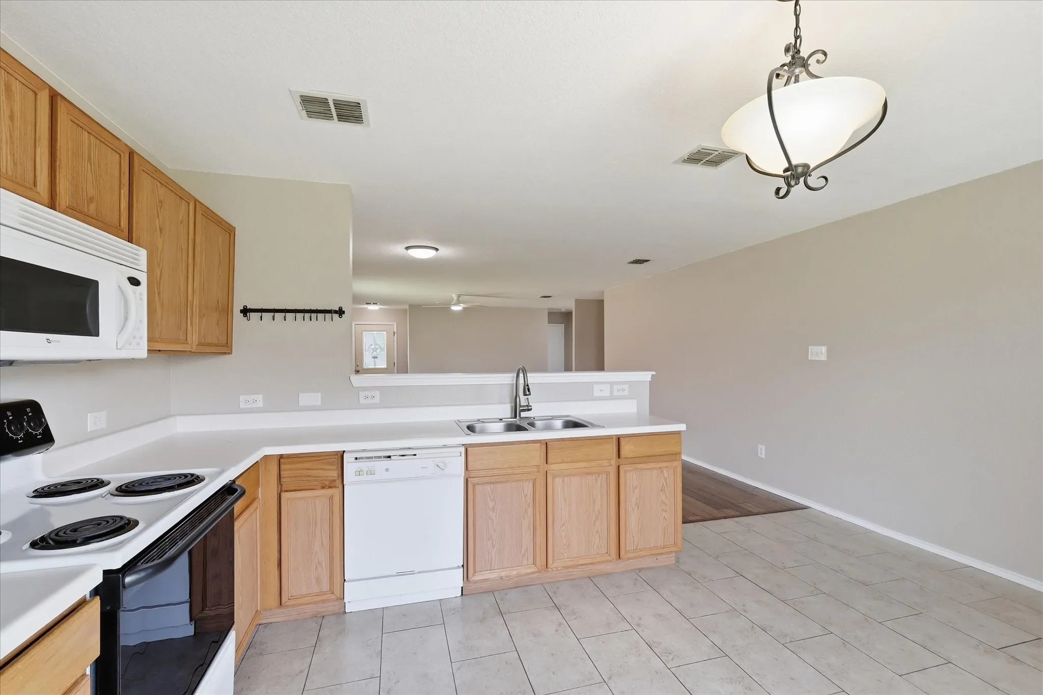 Kitchen featuring light wood cabinetry, white countertops, a built-in microwave, an electric range, and a double basin sink