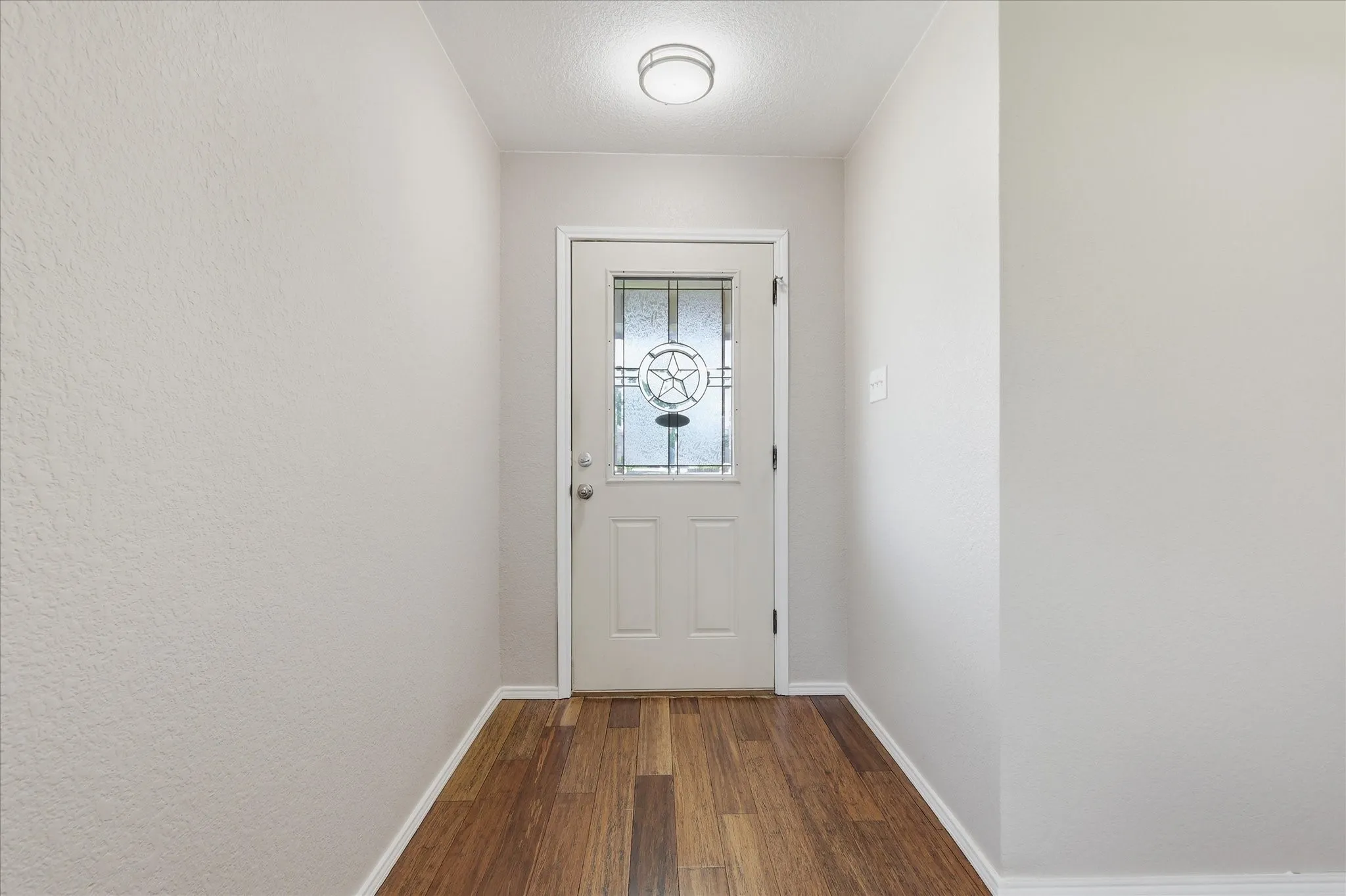 Entryway featuring wood-finish flooring, light-toned walls, and a white door with decorative glass inserts
