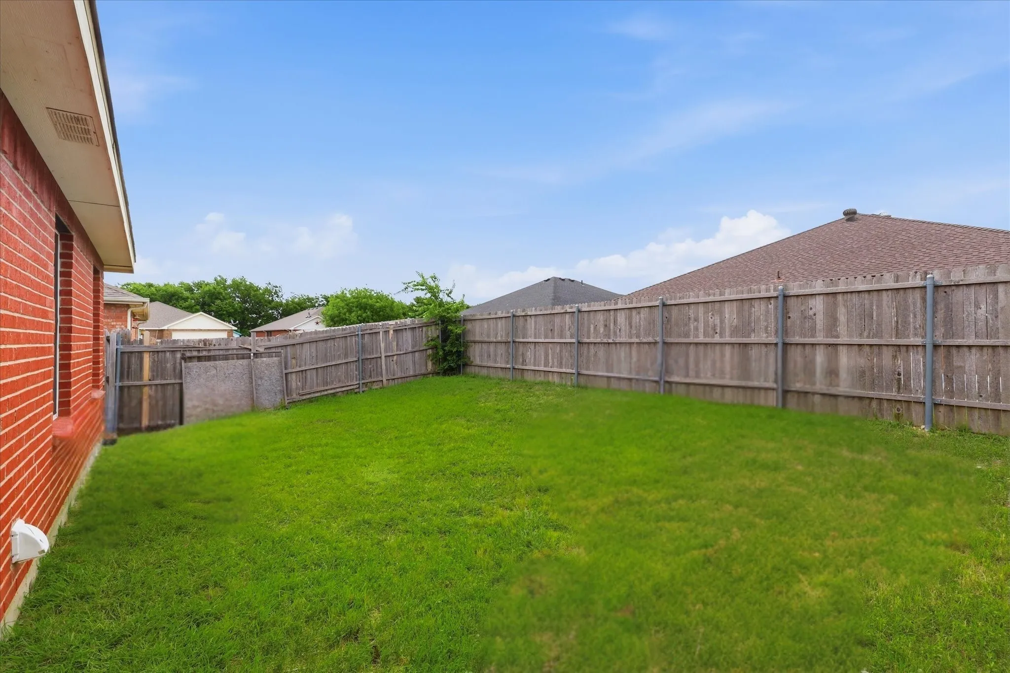 Expansive backyard featuring a manicured lawn, full wood privacy fencing, and brick exterior siding