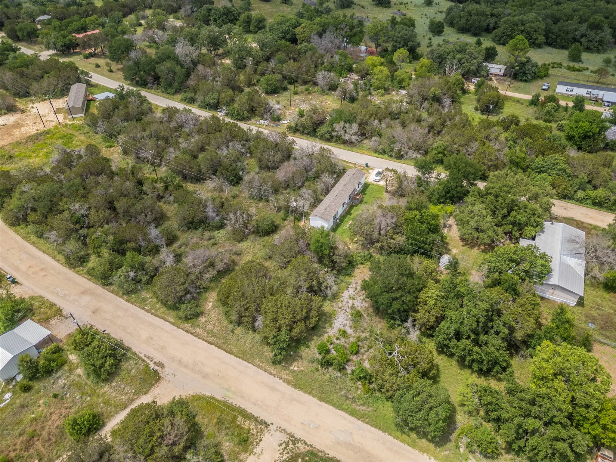 Expansive undeveloped land with two visible dirt roads, scattered mature trees, and a distant metal-roofed structure