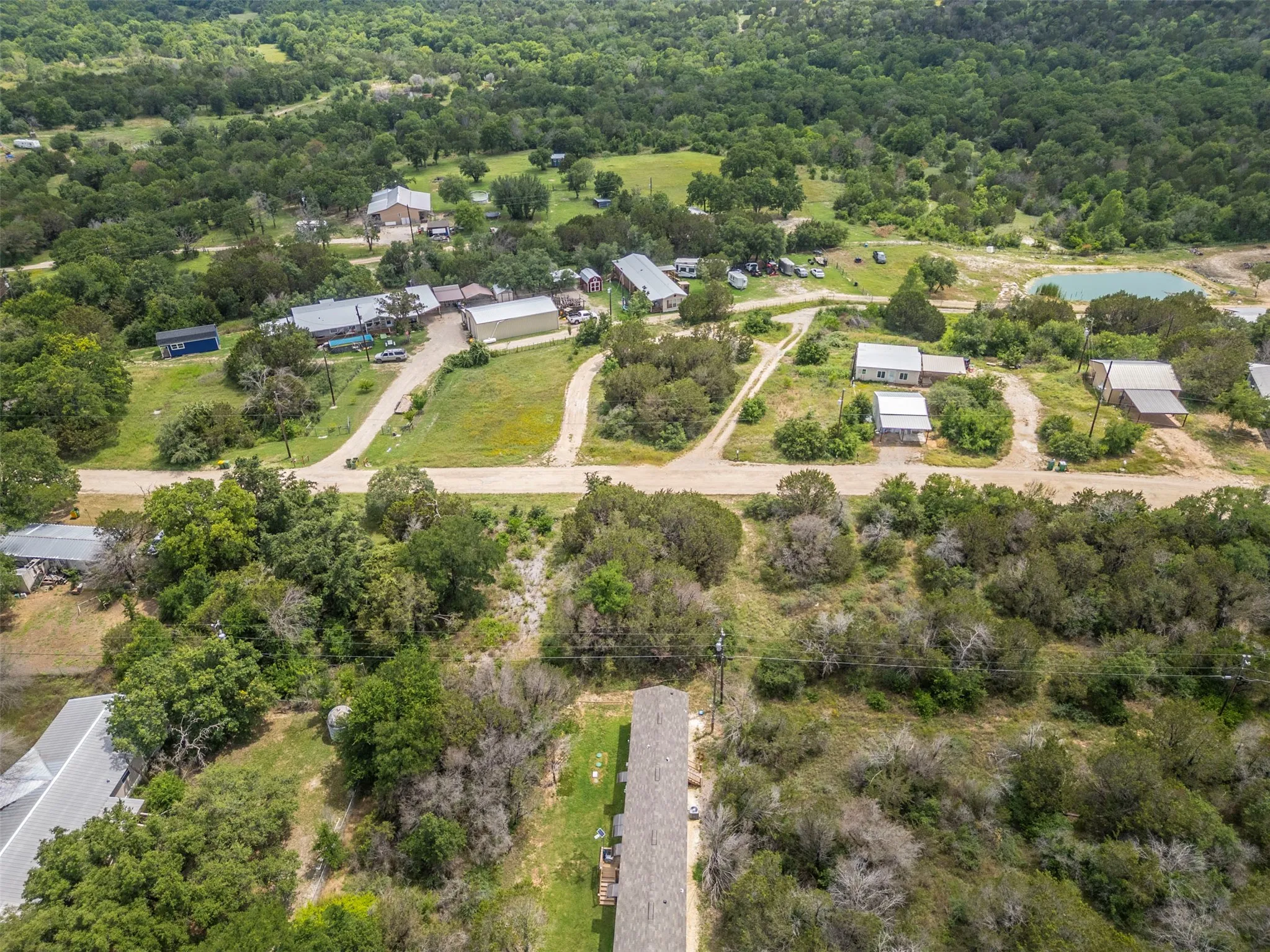 Expansive acreage featuring mature trees, multiple structures with various rooflines, undeveloped land sections, and a visible pond
