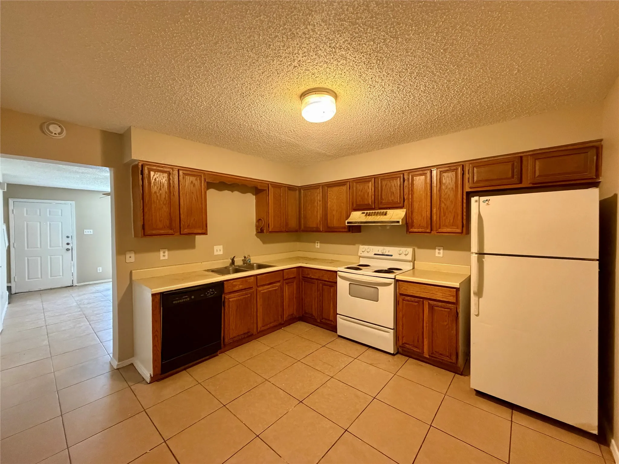 Kitchen featuring wood cabinetry, laminate countertops, tile flooring, a built-in dishwasher, and a refrigerator