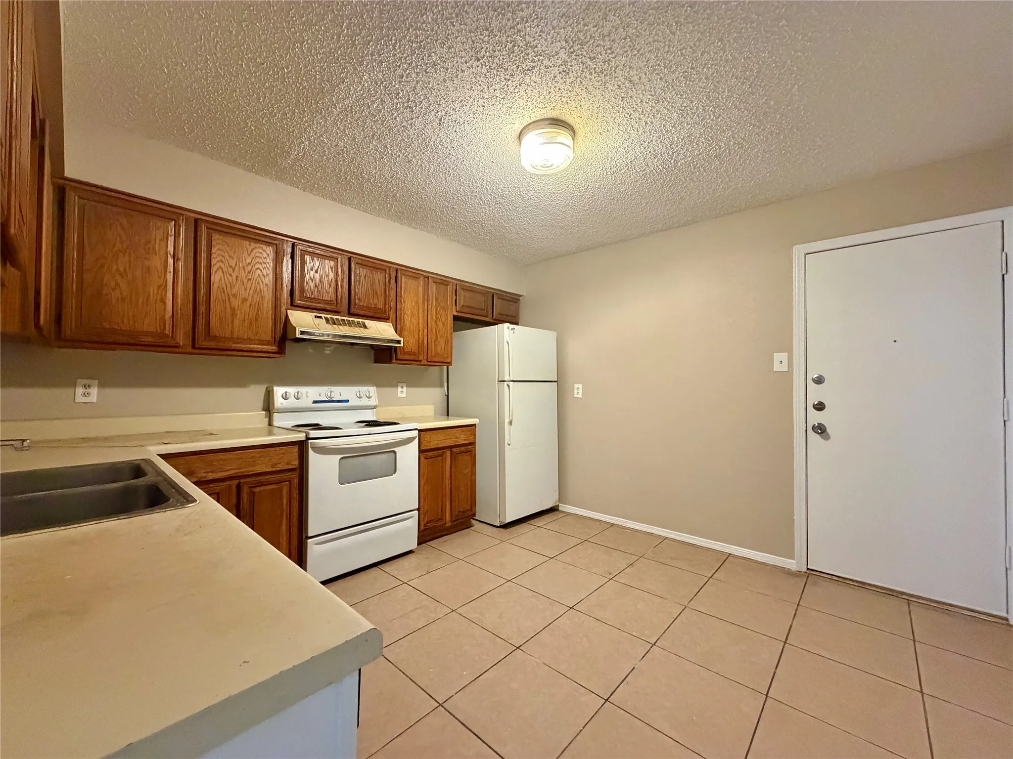 Kitchen with wood cabinetry, light-toned countertops, a double basin sink, and tile flooring