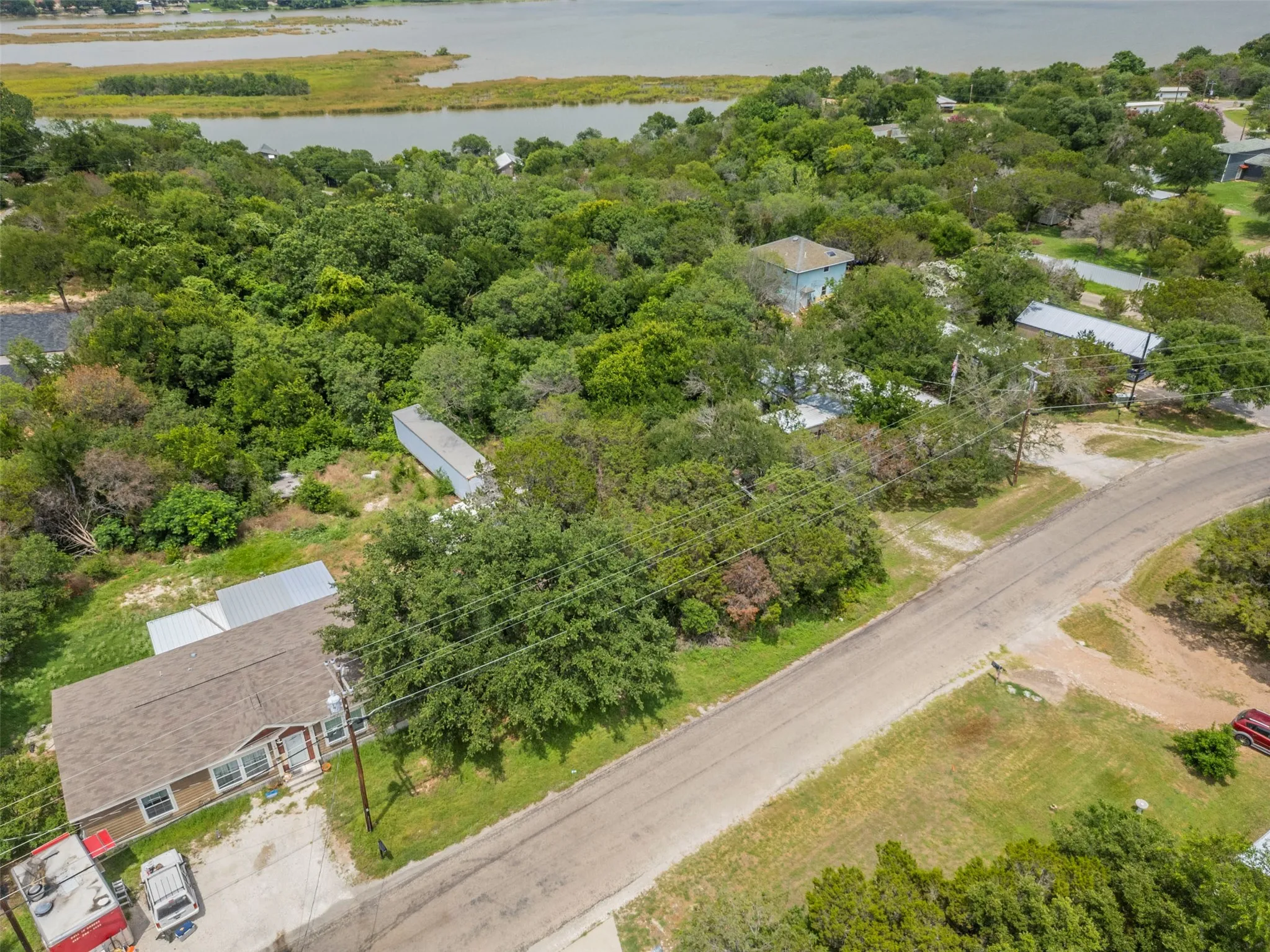 Aerial perspective showcasing a property surrounded by mature trees, featuring a visible road, and distant water