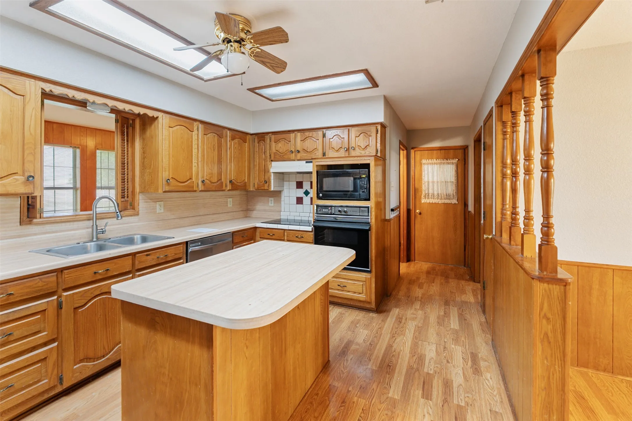 Kitchen featuring wood-finish flooring, oak cabinetry, a center island with countertop, skylights, and built-in appliances