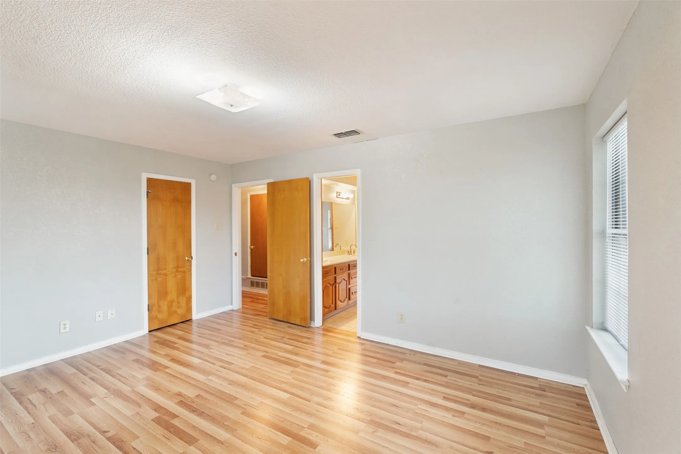 Spacious room featuring wood-finish flooring, light grey painted walls, a window with blinds, and recessed lighting