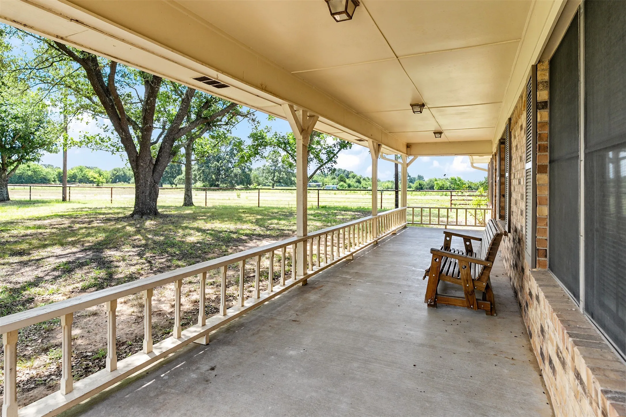 Spacious covered front porch with concrete flooring and wood railings