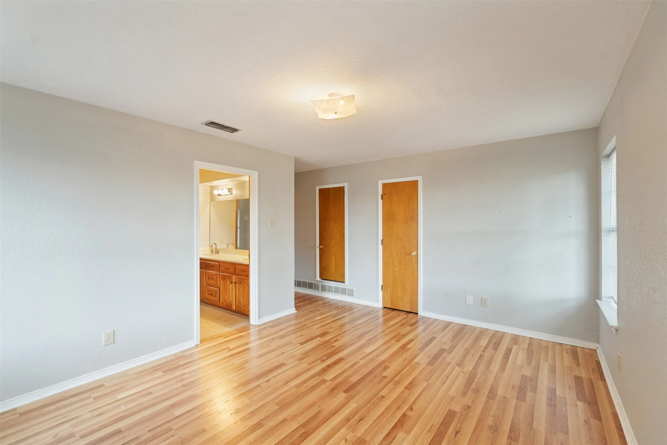 Spacious interior room featuring wood-finish flooring, light gray wall paint, and a semi-flush ceiling light fixture