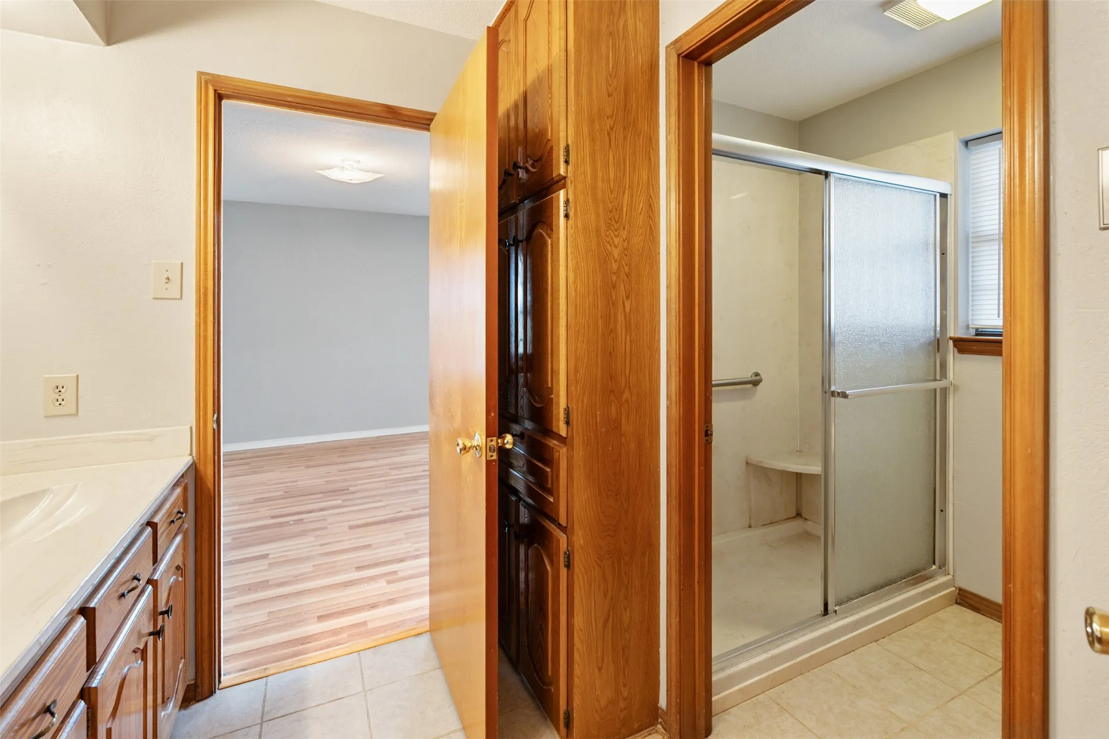 Bathroom featuring a wood vanity with a white countertop, built-in wooden cabinetry, and a shower with a sliding glass door and integrated seating