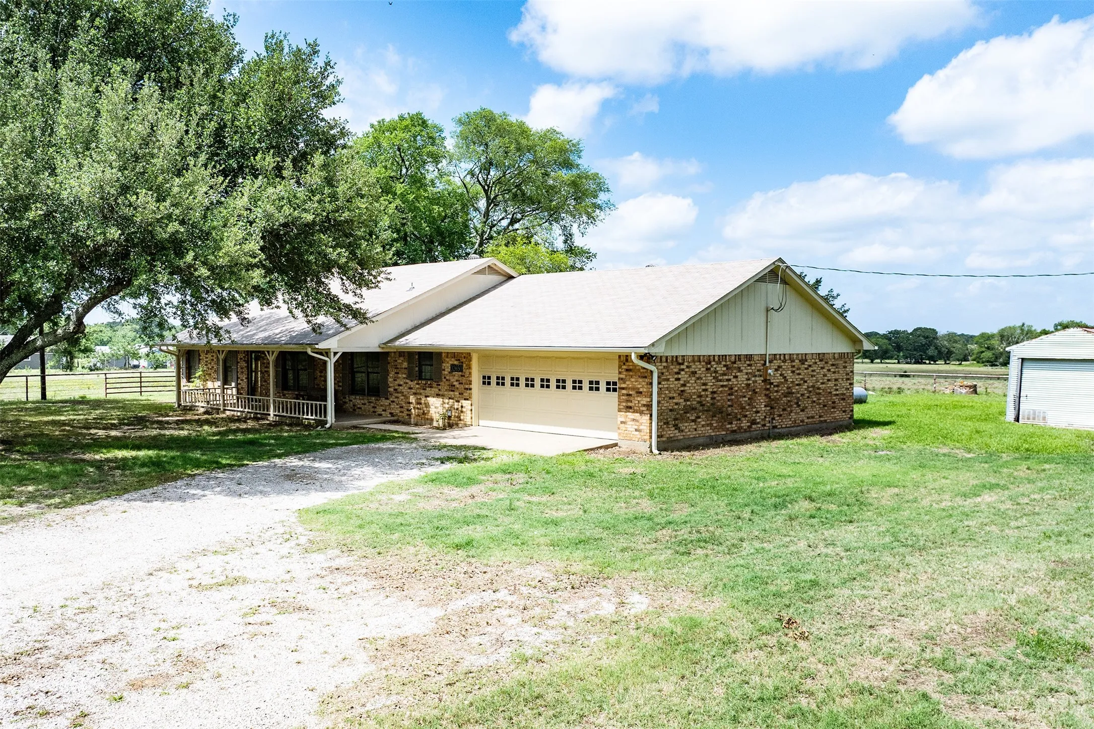 Brick exterior residence featuring a two-car garage with panel doors, a covered front porch, and a gravel driveway