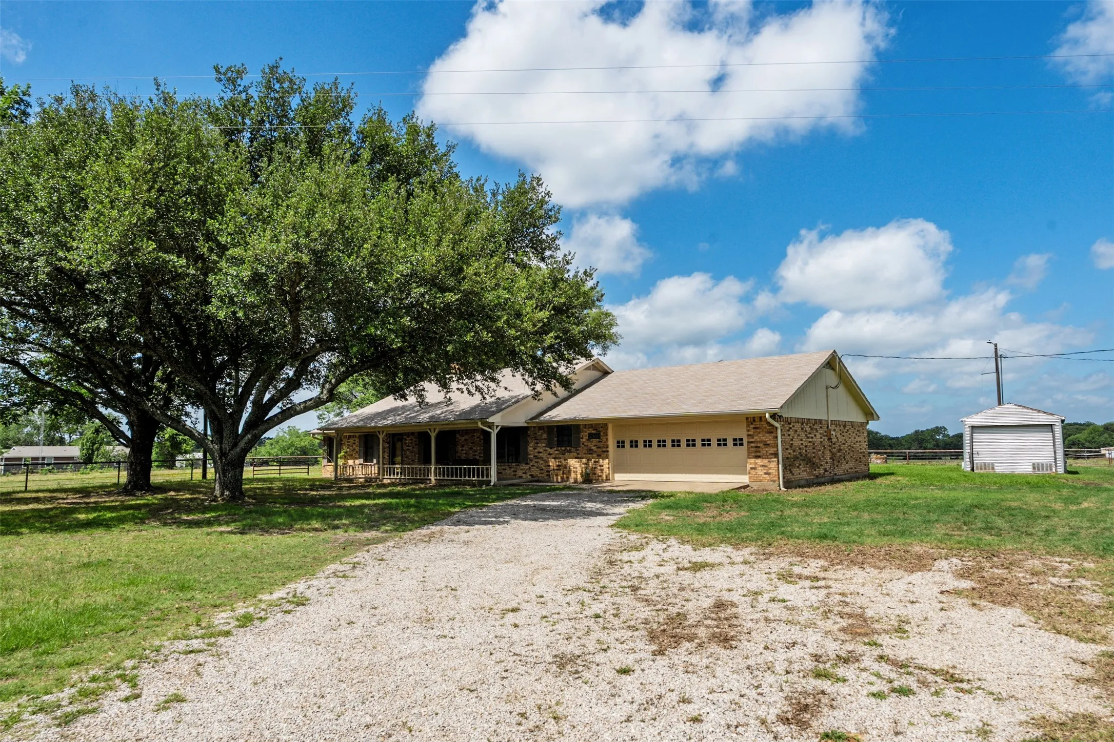 Ranch-style residence featuring a gravel driveway, mature trees, a brick and siding exterior, an attached two-car garage, and a separate storage shed