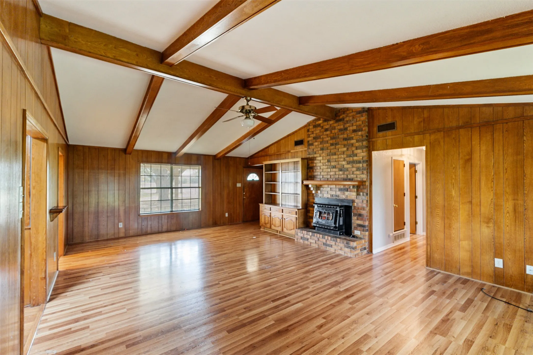 Spacious interior featuring wood-finish flooring, wood-paneled walls, and a vaulted ceiling with exposed wood beams