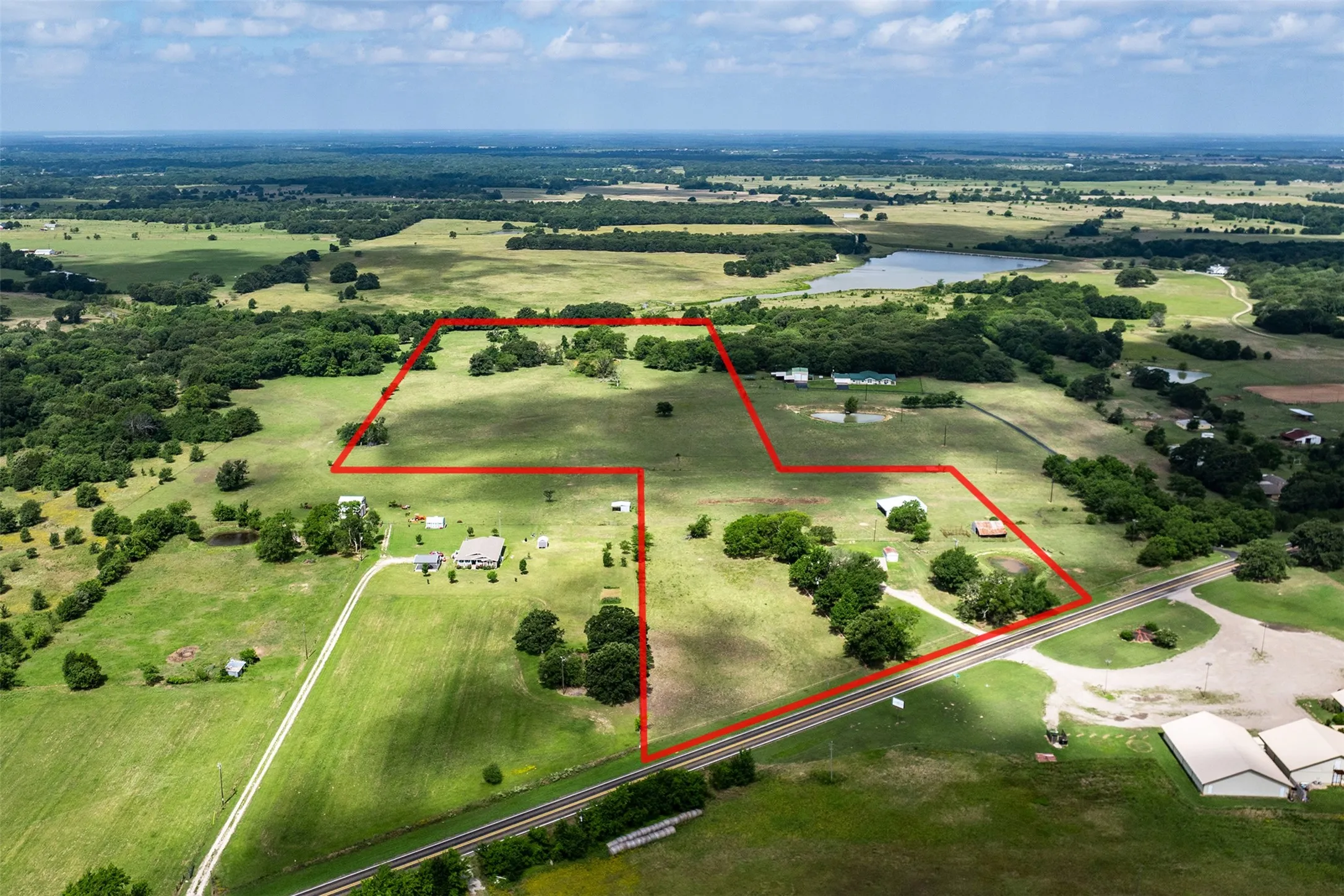 Expansive land parcel featuring multiple structures, open pastures, mature trees, a private pond, and direct road frontage