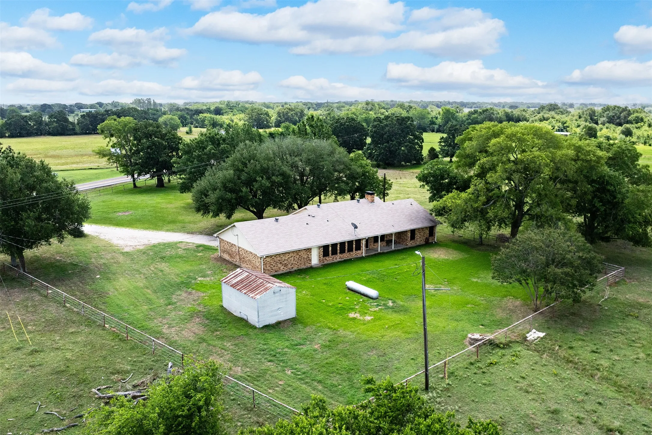 Expansive rural property featuring a brick exterior structure with a covered porch, surrounded by mature trees and lush greenery