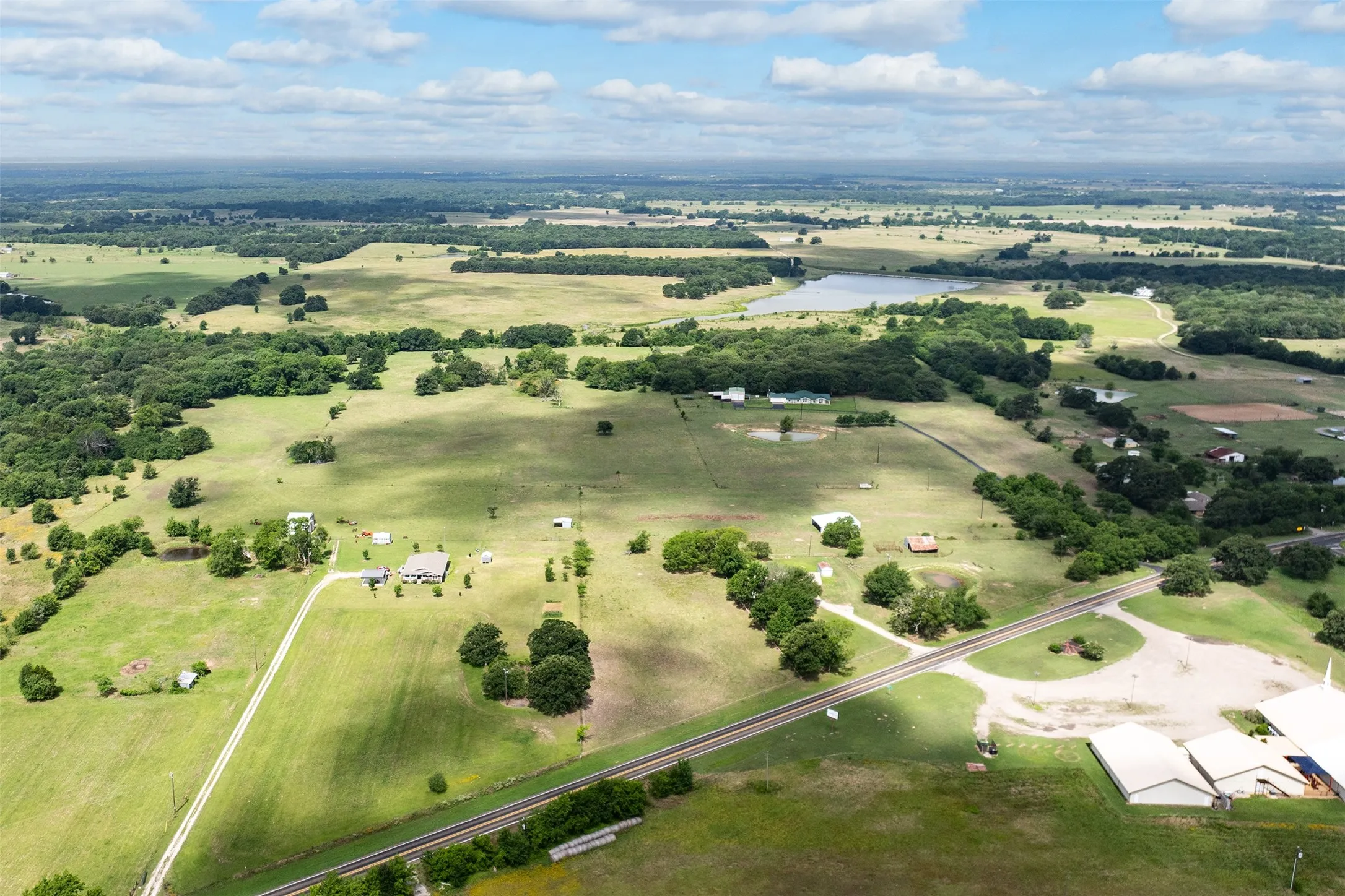 Expansive rural landscape featuring scattered trees, open fields, and a prominent body of water