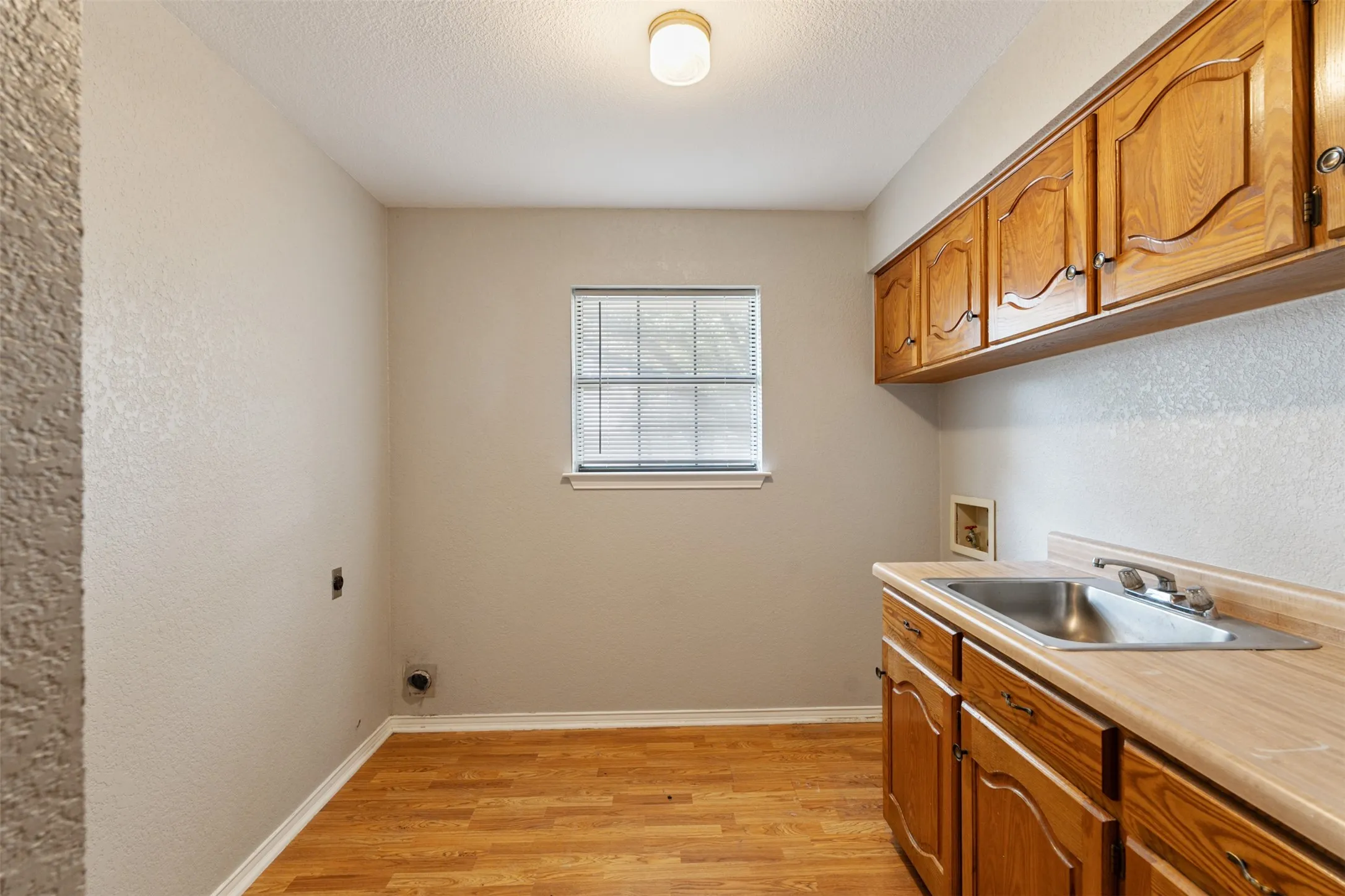 Utility room featuring wood-finish flooring, a single window, and a built-in sink with cabinetry