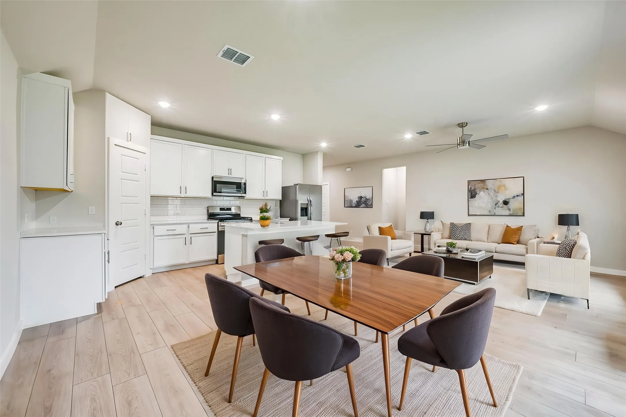 Kitchen featuring white shaker-style cabinetry, a large kitchen island with an undermount sink and gooseneck faucet, light-toned countertops, a stainless steel side-by-side refrigerator, and wood-finish flooring