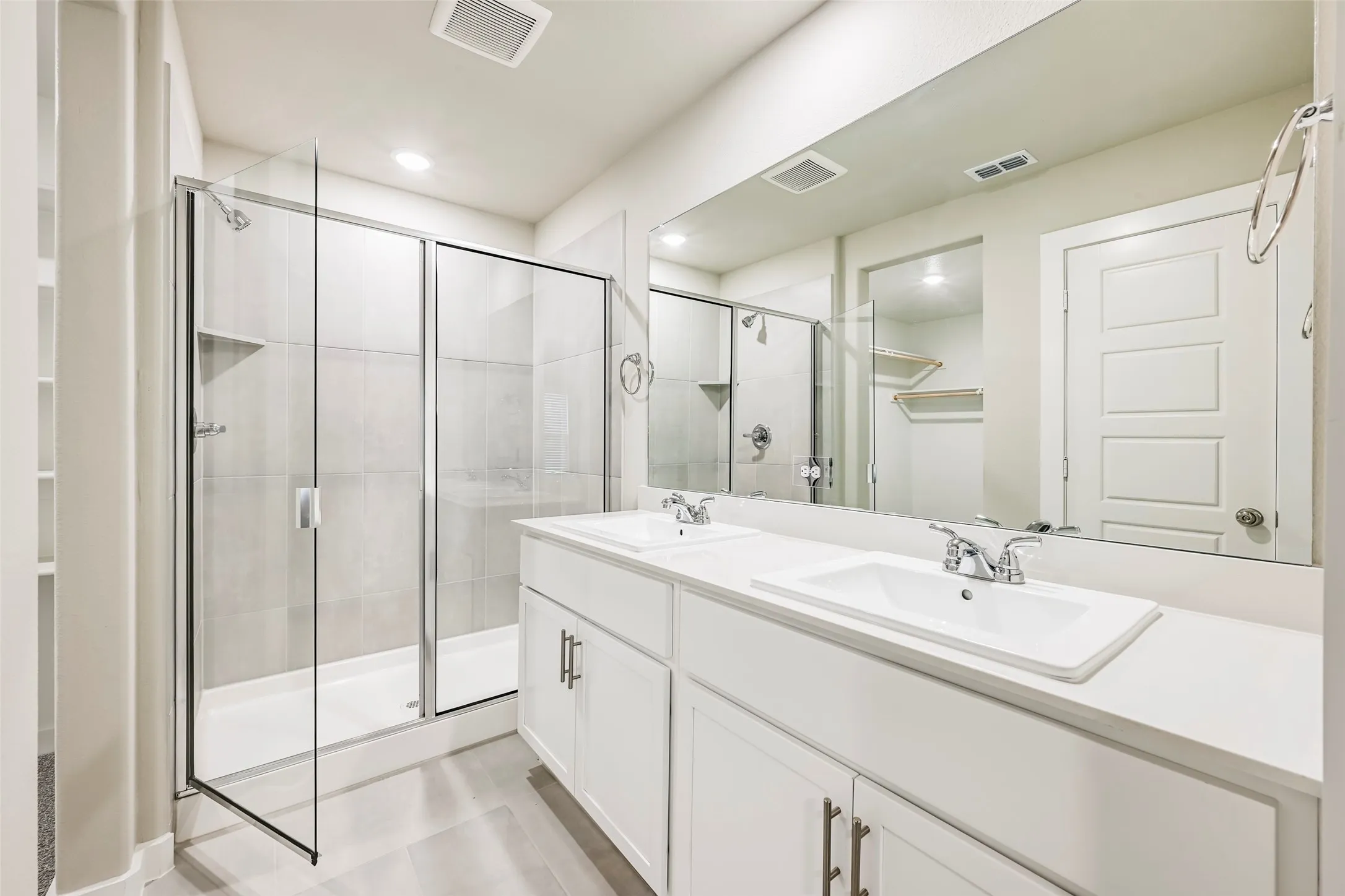 Bathroom featuring a dual vanity with undermount sinks, a spacious glass-enclosed shower with a tiled surround, and a large mirror