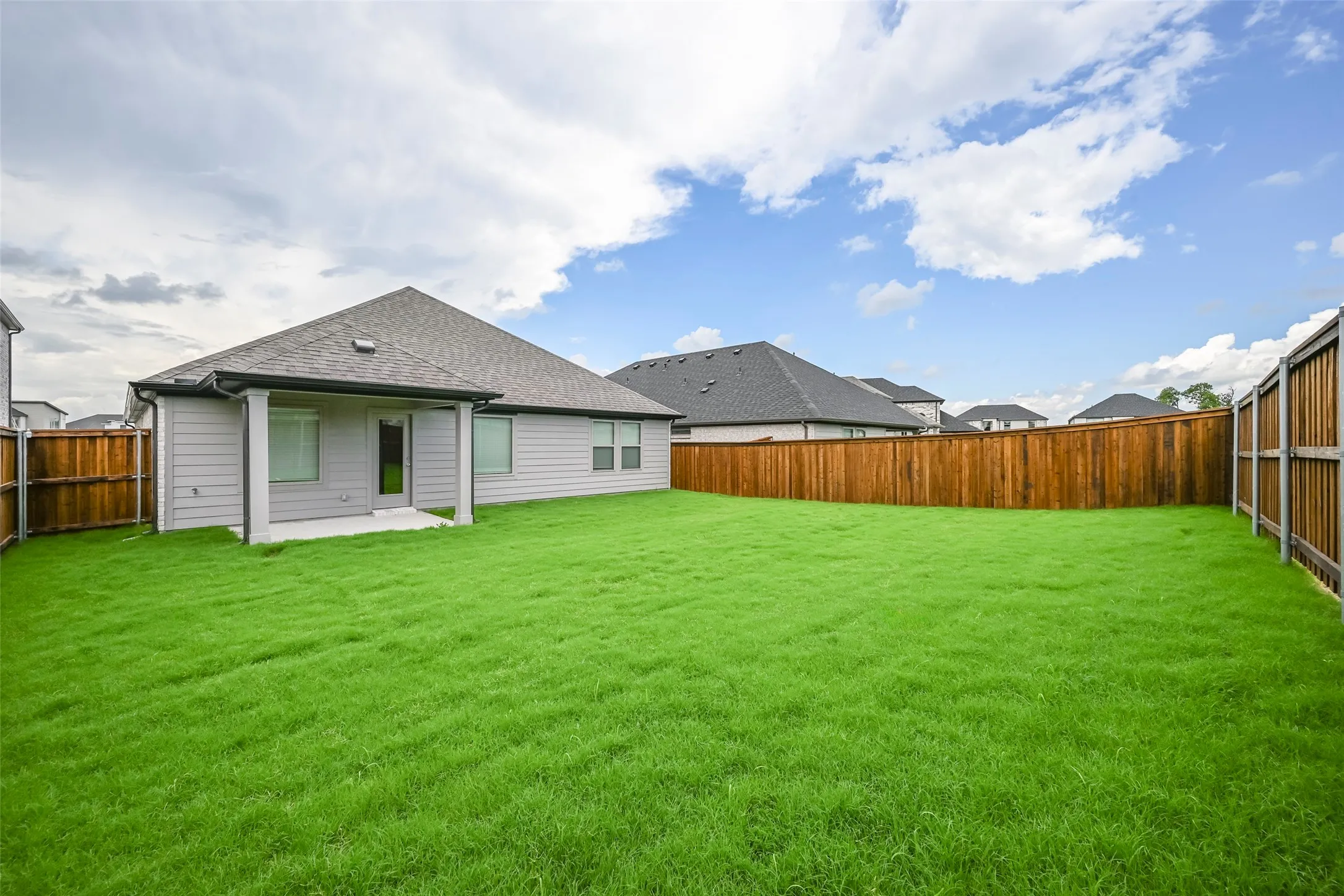 Expansive backyard featuring a manicured lawn, a full wood privacy fence, and a covered concrete patio