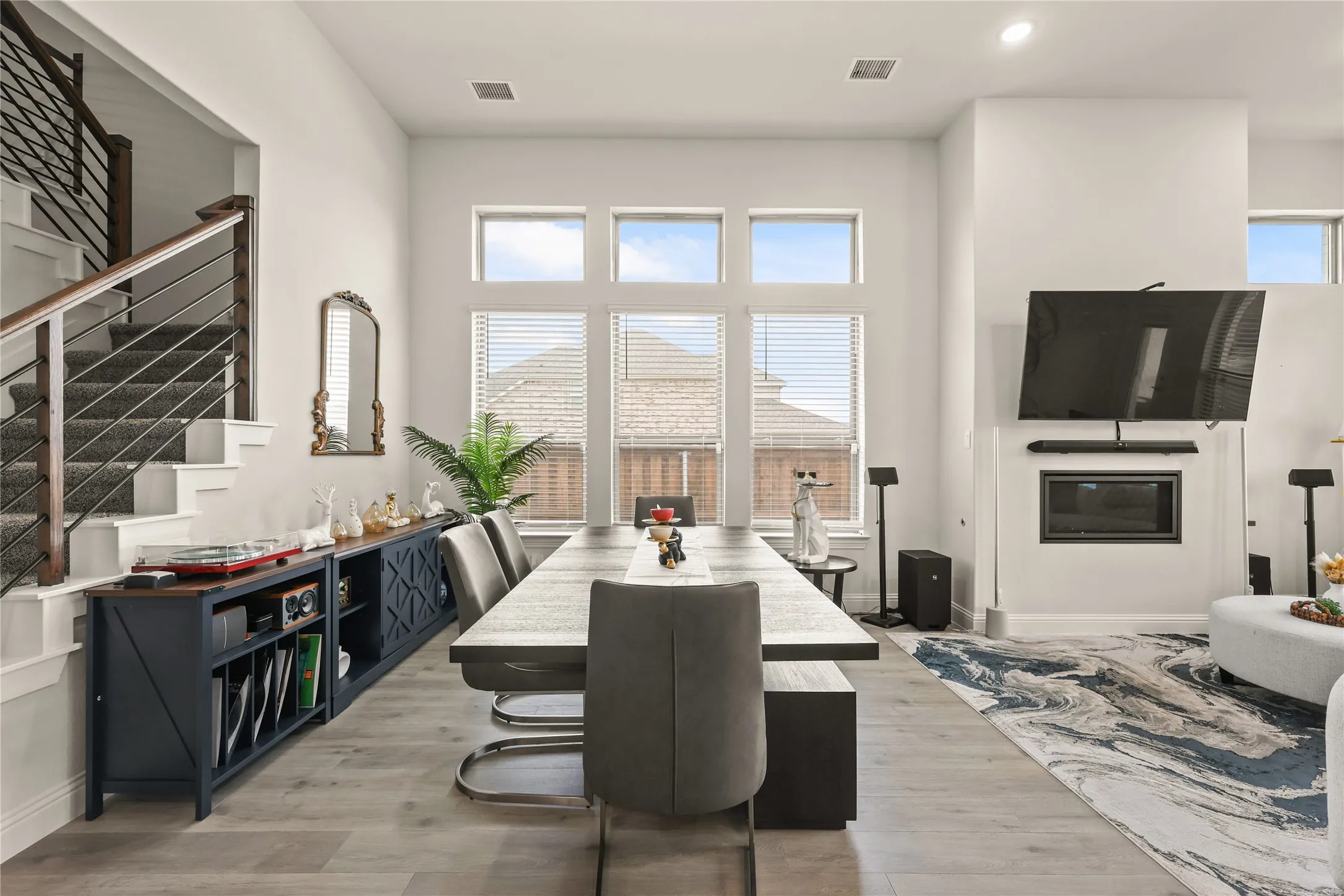 Open-concept living area featuring high ceilings, wood-finish flooring, a contemporary fireplace, and a striking staircase with dark metal balusters and a wood handrail