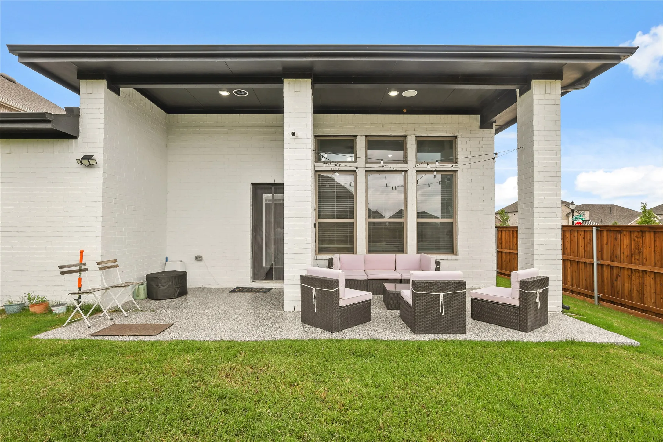 Rear covered patio featuring a white brick exterior, a dark soffit, recessed lighting, a concrete-finish patio floor, and a wooden fence perimeter