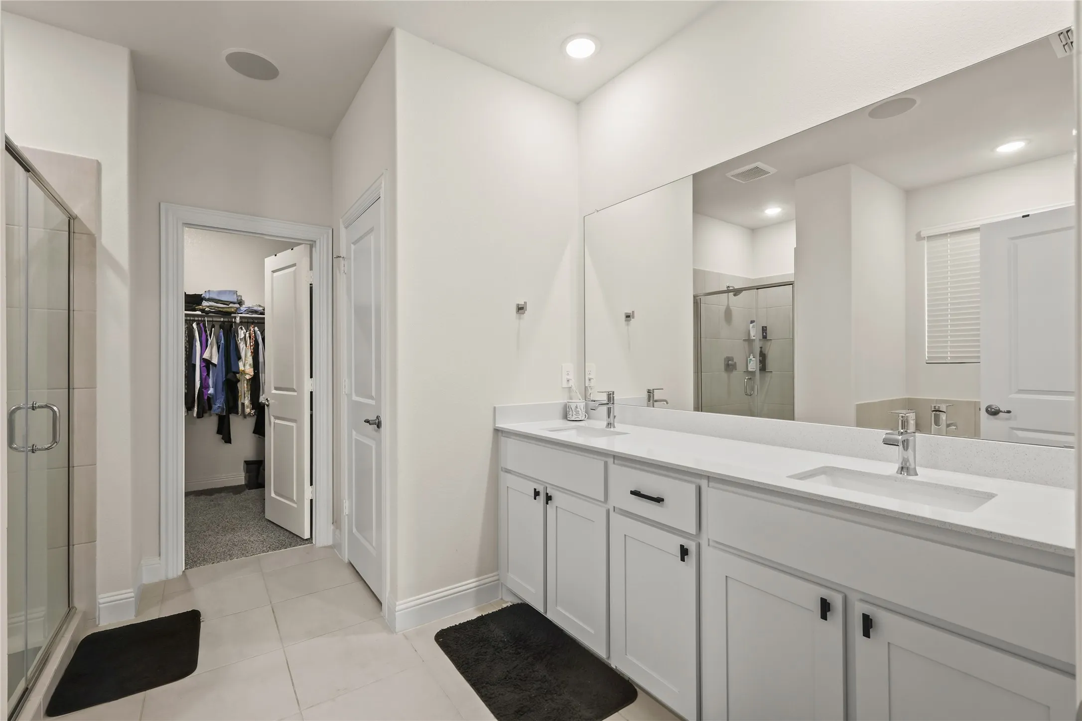 Bathroom featuring a dual vanity with white cabinetry, light-colored countertops, and chrome fixtures